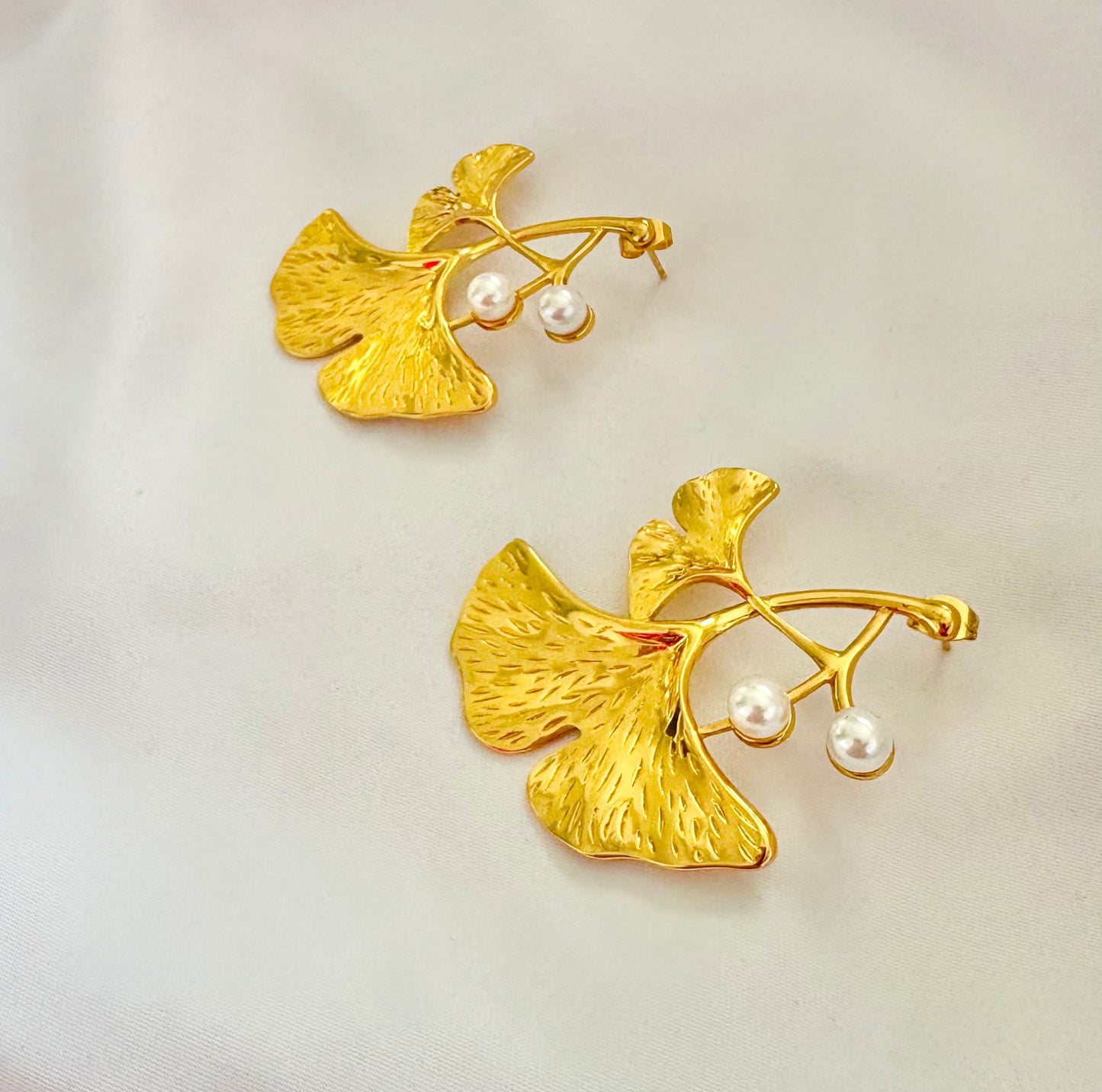 Gold leaf-shaped earrings with pearl-like beads on a light background