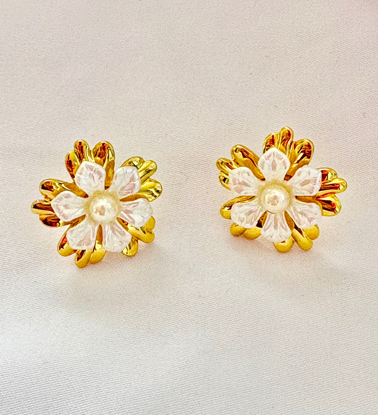 Pair of floral earrings with gold and white design on a light background