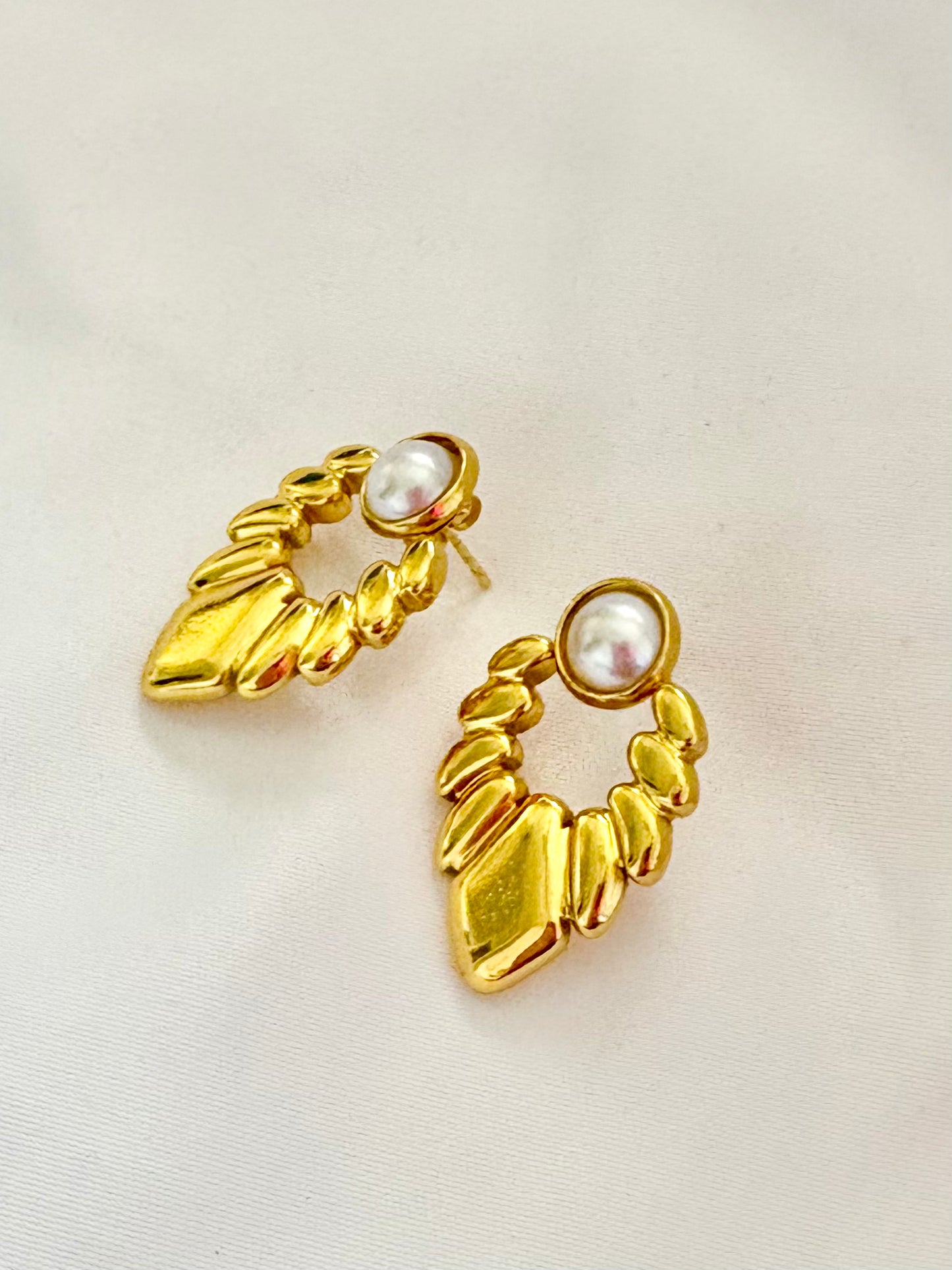 Gold earrings with pearl-like stones on a light beige background