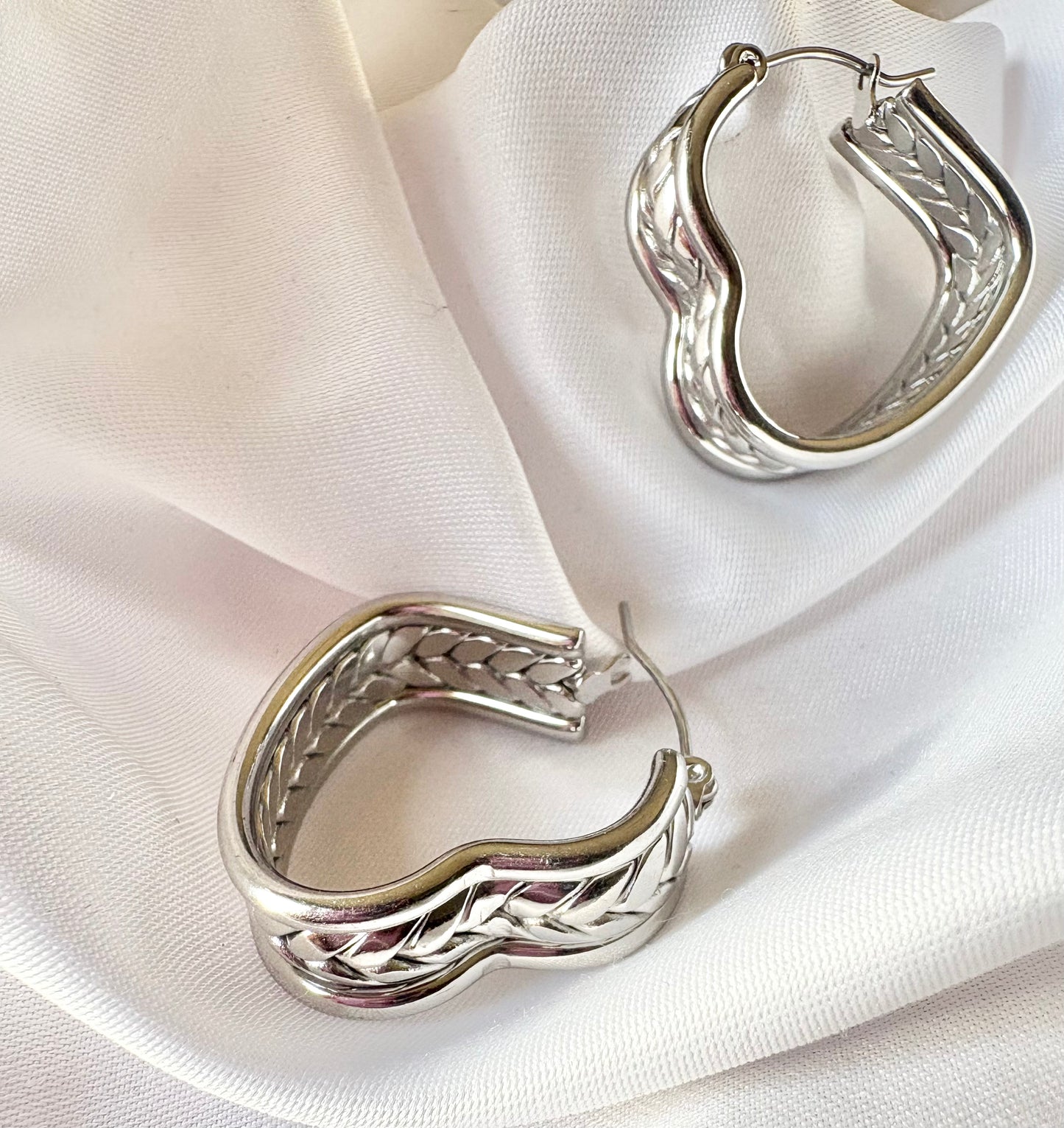 Silver hoop earrings with braided design on a white fabric background