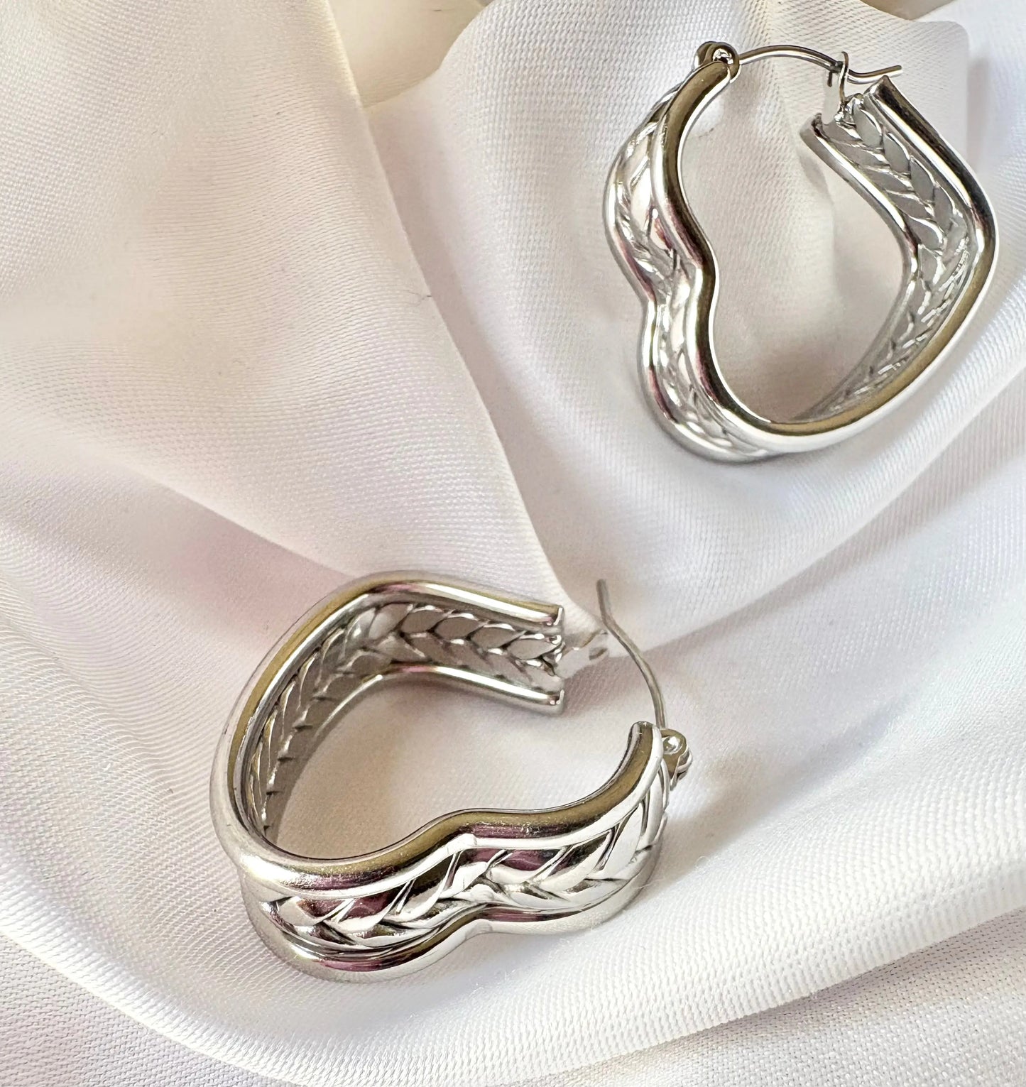 Silver hoop earrings with braided design on a white fabric background