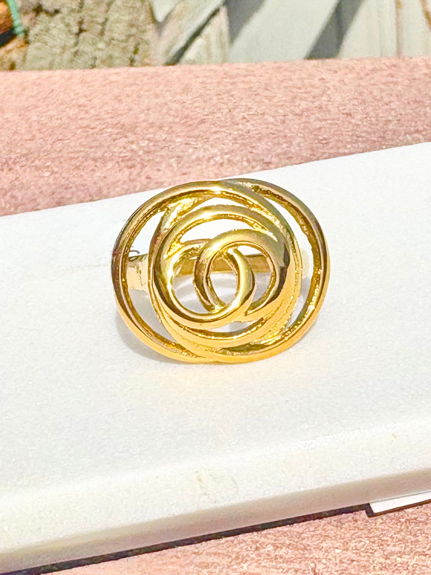 Gold spiral ring on a white surface with a pink background