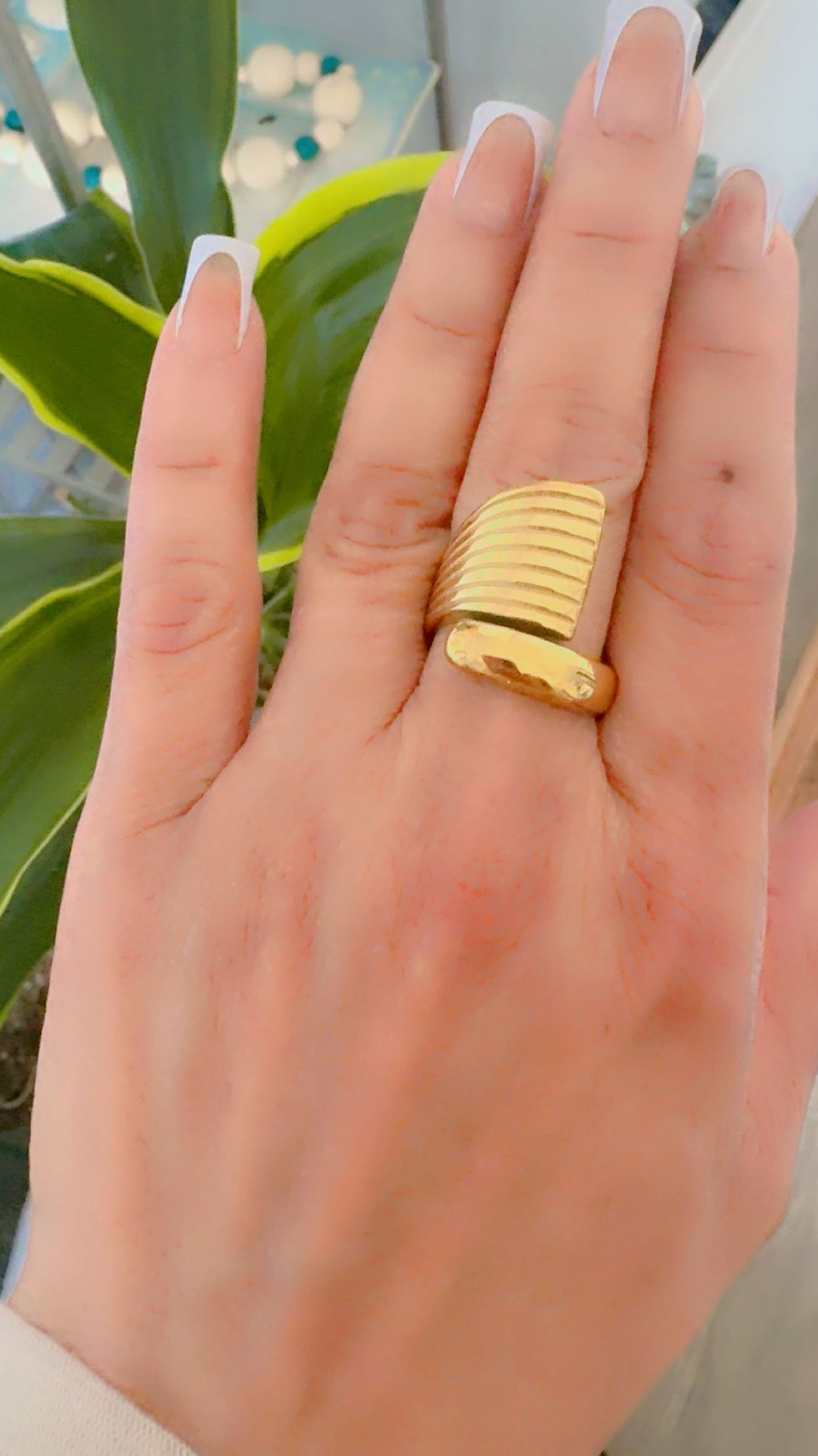 A close-up of a hand wearing a wide, chunky gold ring with horizontal ridges.