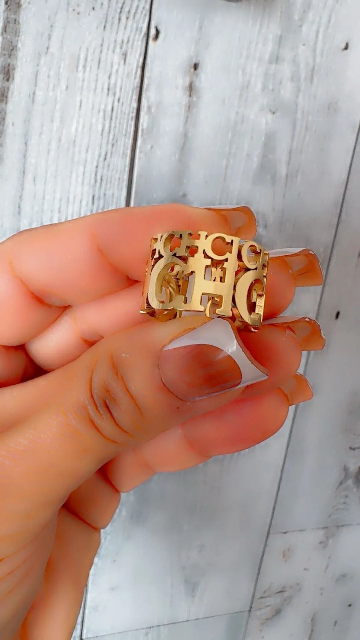 Gold ring with 'CH' letters held by a hand against a light wooden background