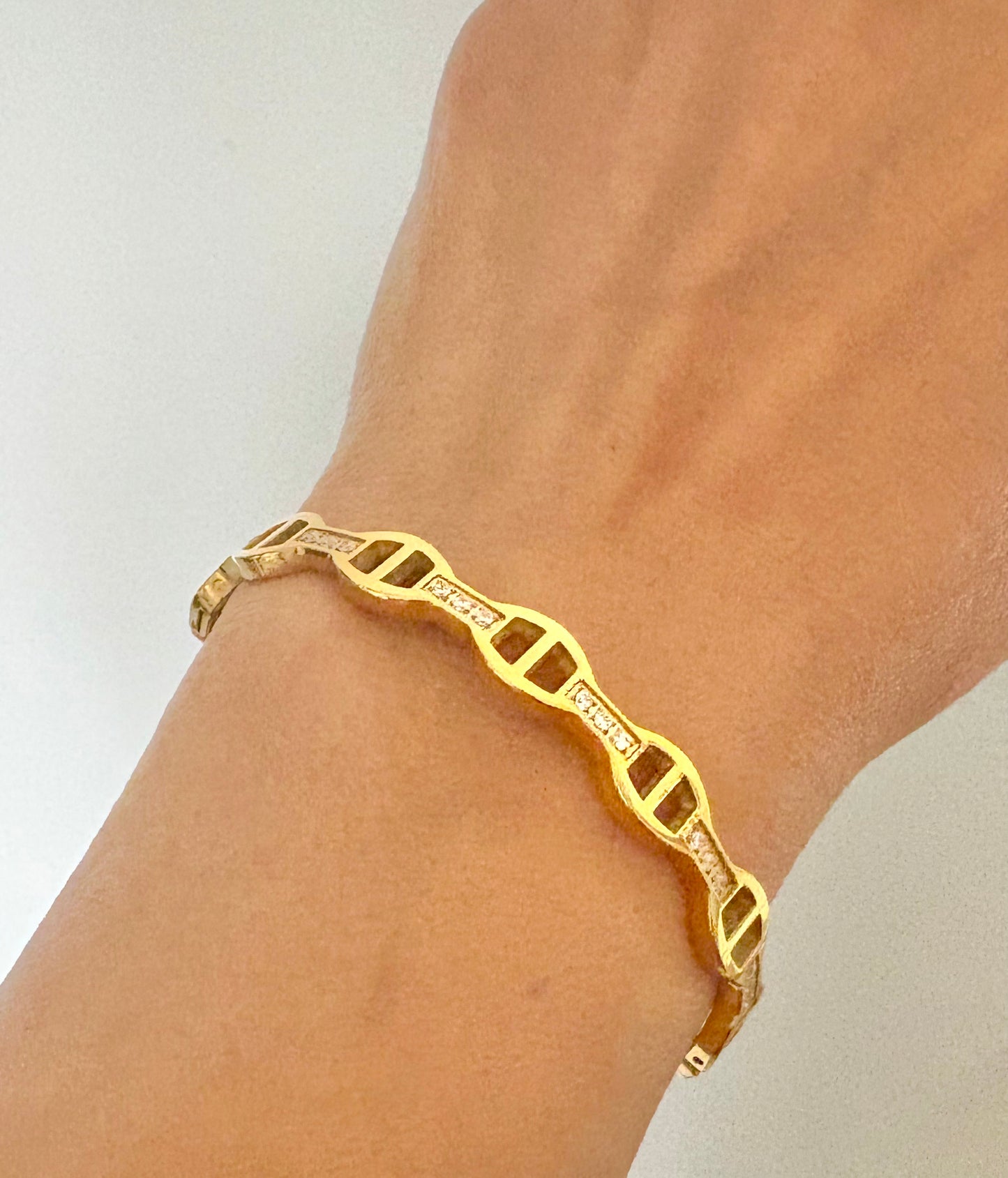 Gold bracelet on a wrist with a plain background