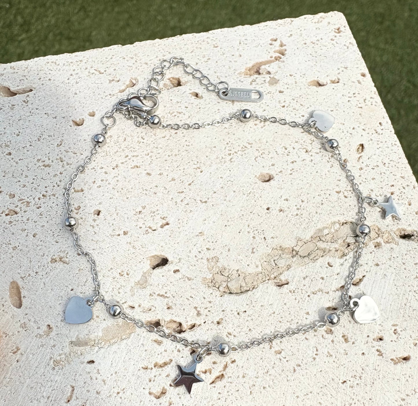 Silver anklet with heart and star charms on a textured surface