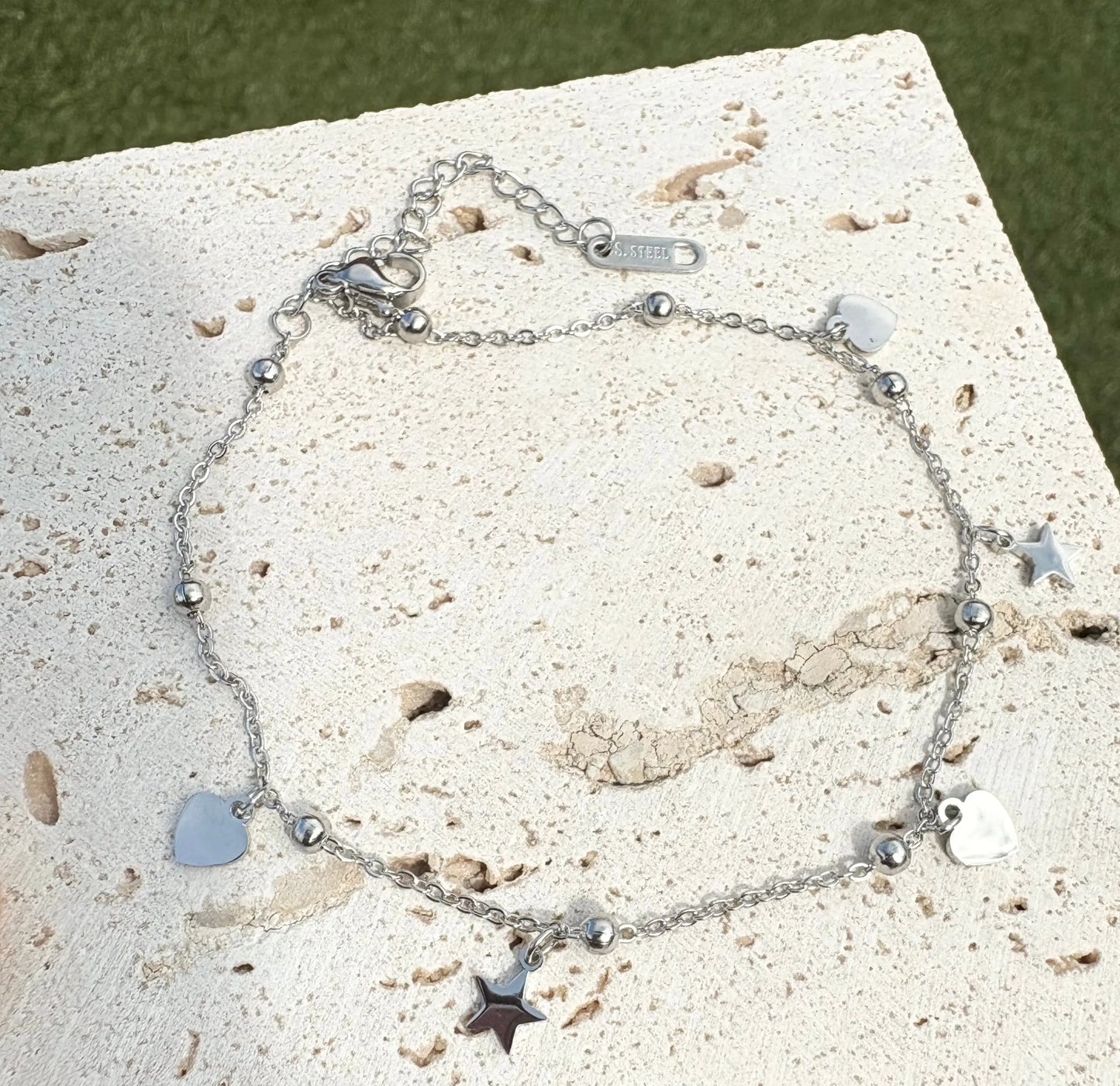 Silver anklet with heart and star charms on a textured surface