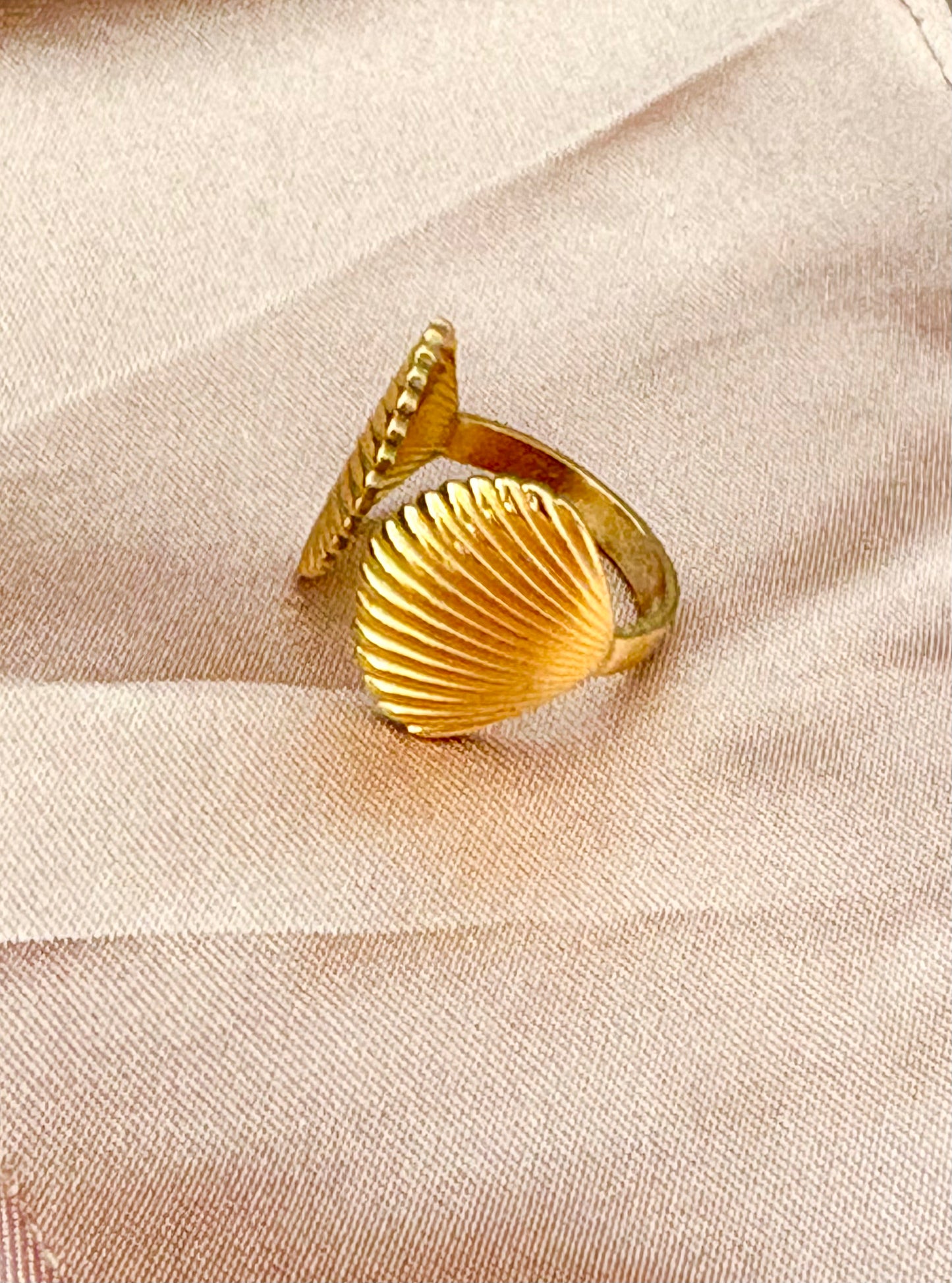 Gold shell-shaped ring on a beige fabric background