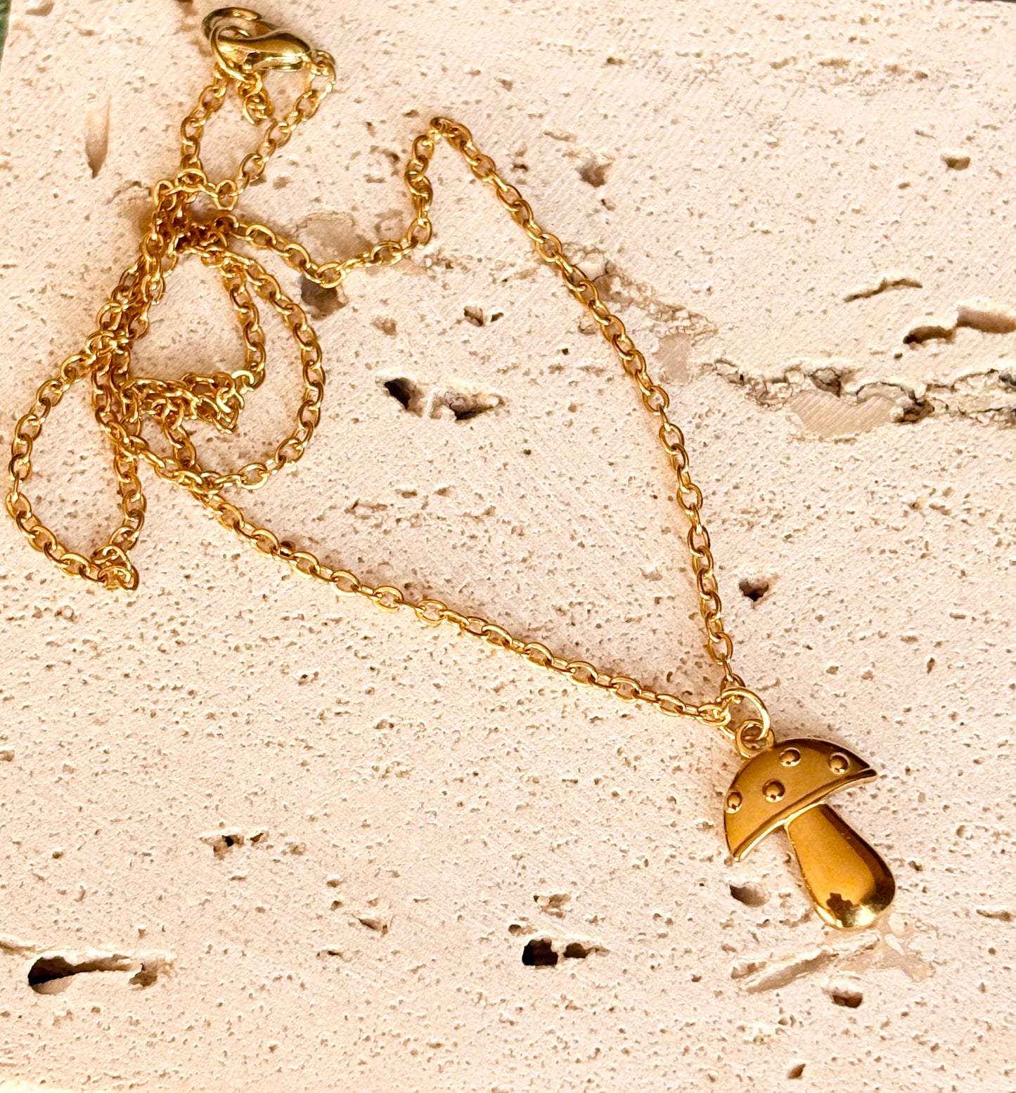 Gold necklace with a mushroom pendant on a textured beige surface