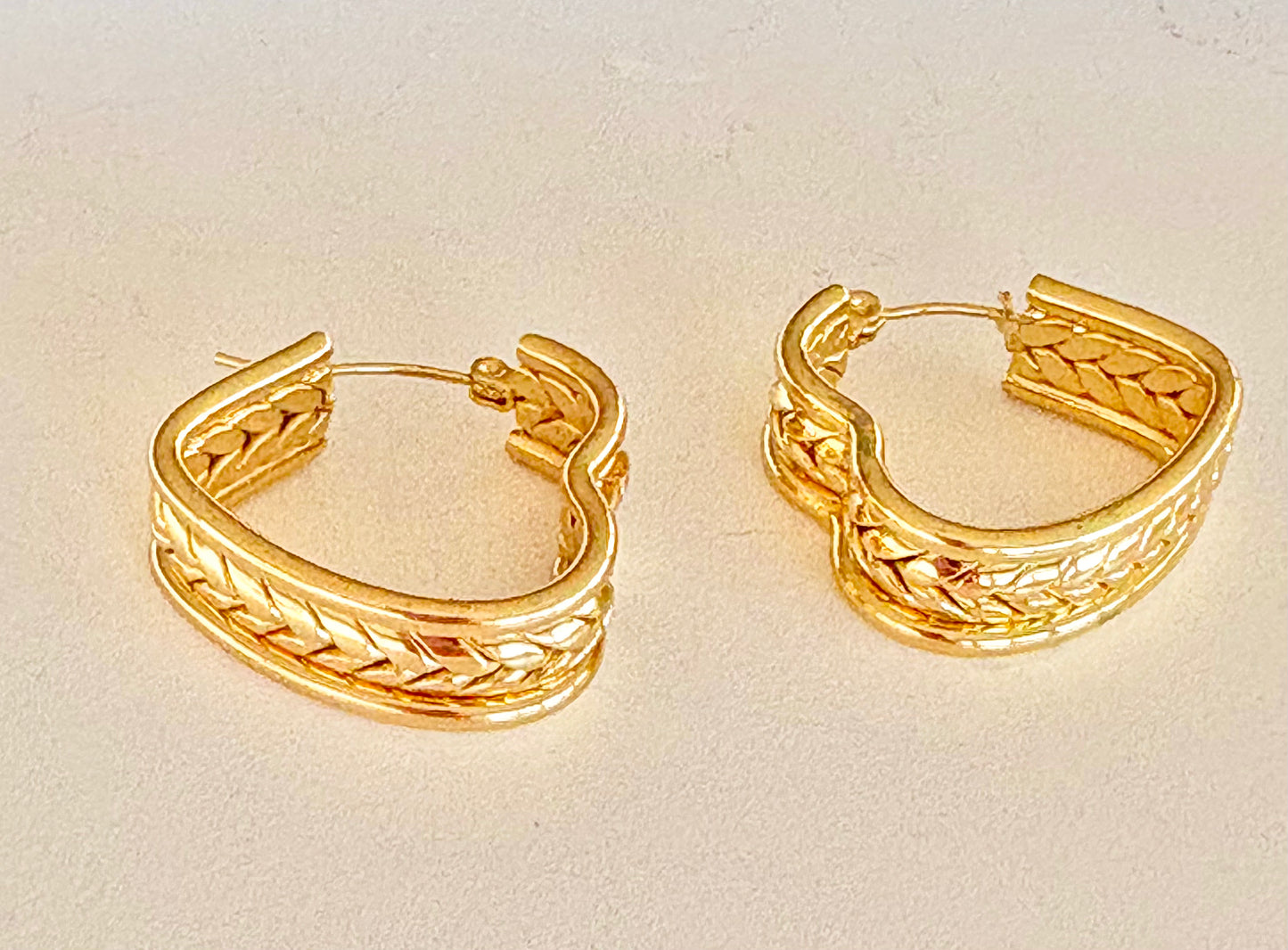 Gold and silver braided hoop earrings laid flat, showing the curved wave shape and 2.5 cm size