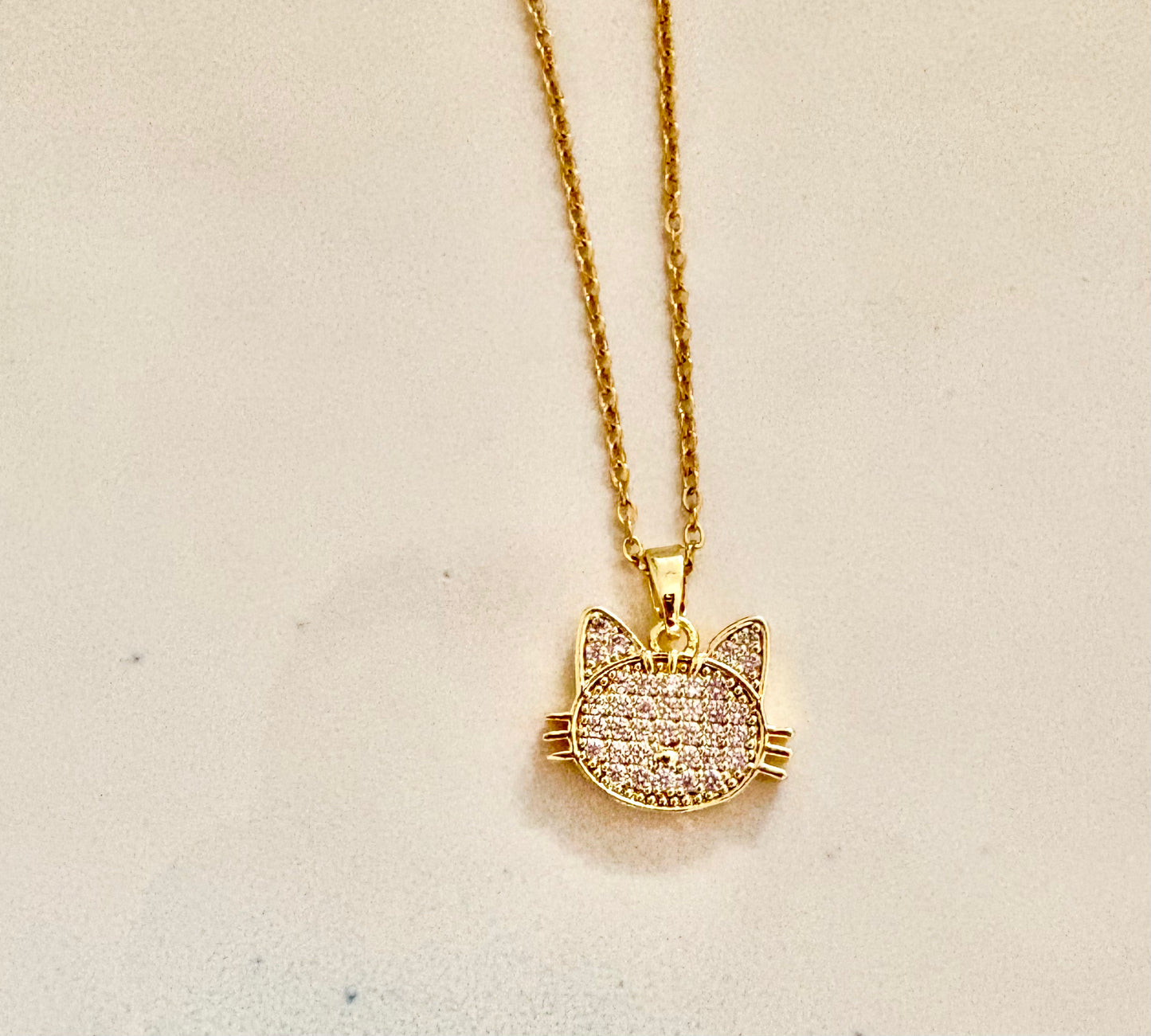 Gold cat-shaped pendant necklace on a light beige background
