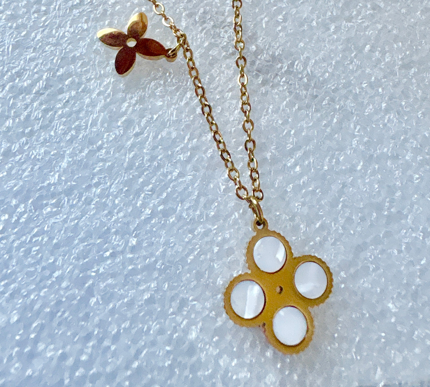 Layered clover necklace featuring a four-petal clover pendant and floral charm on a gold chain.