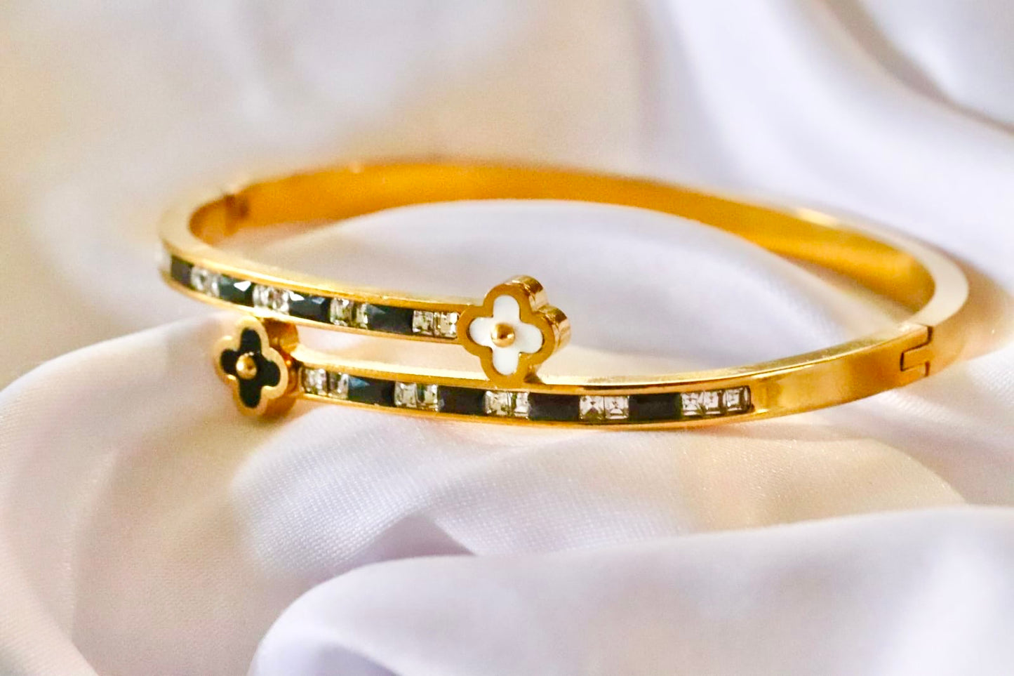 Gold bracelet with clover design on a white fabric background