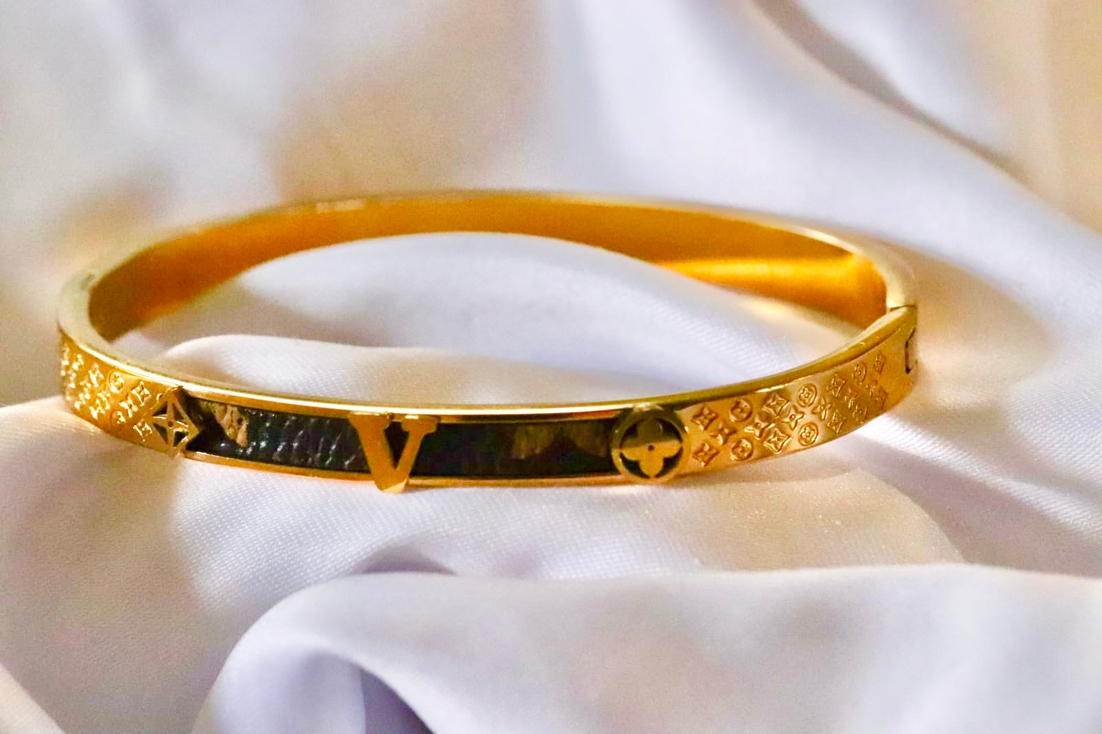 Gold bracelet with intricate designs on a white fabric background