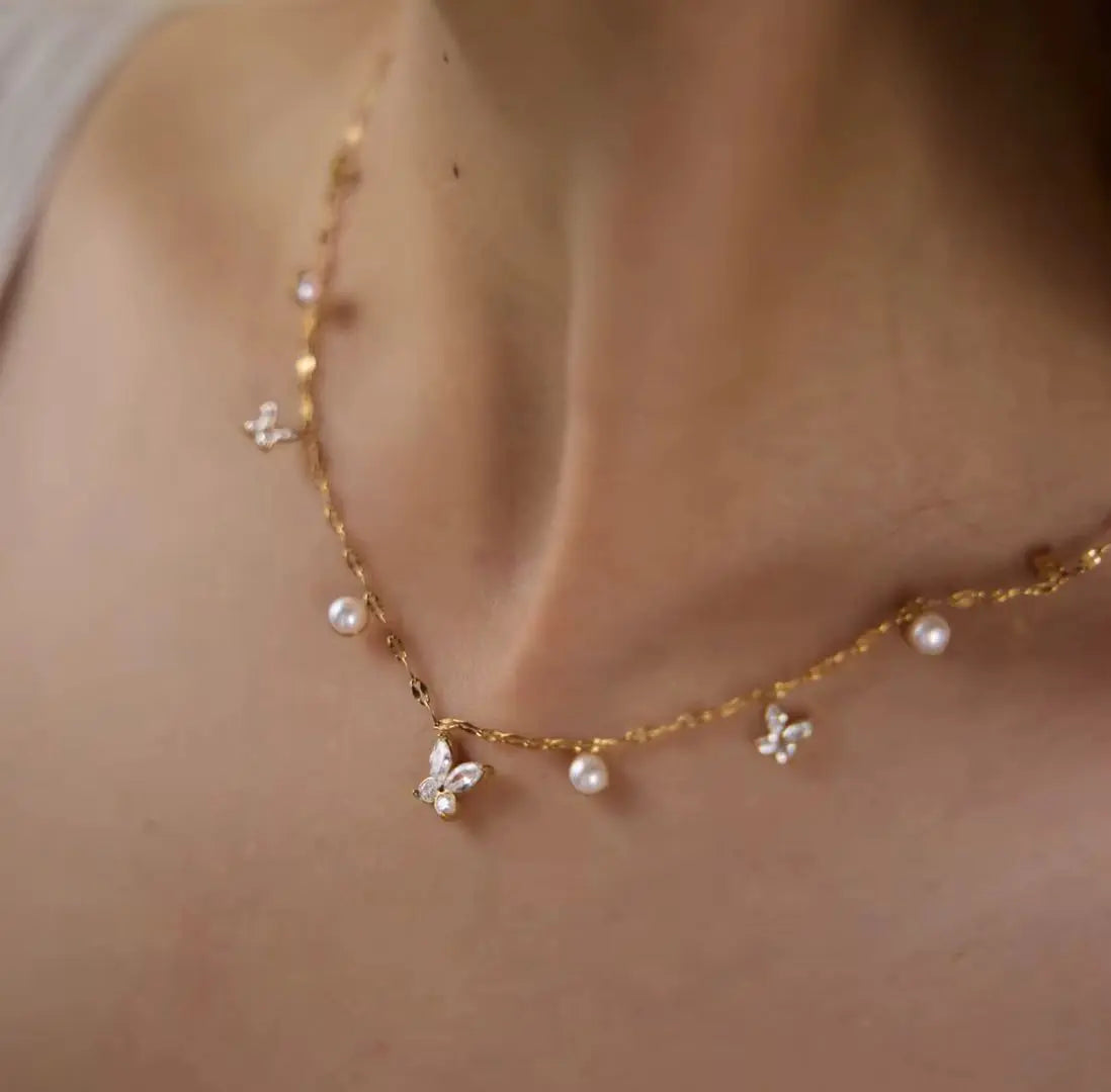 A delicate gold chain necklace featuring small white pearls and butterfly-shaped charms.