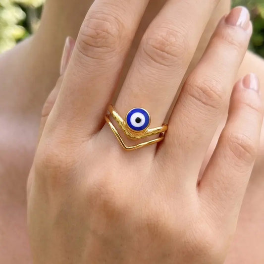 18K gold-plated double chevron ring with a round blue-and-white evil eye detail, shown on a hand
