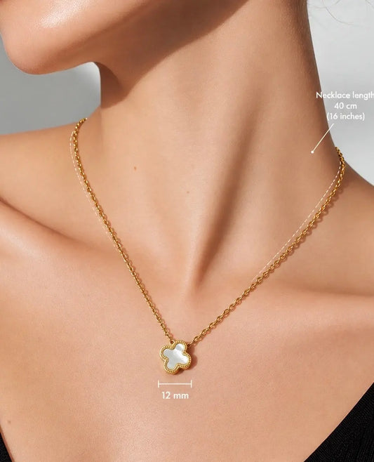 A close-up of a model wearing a delicate gold chain necklace with a small clover-shaped pendant