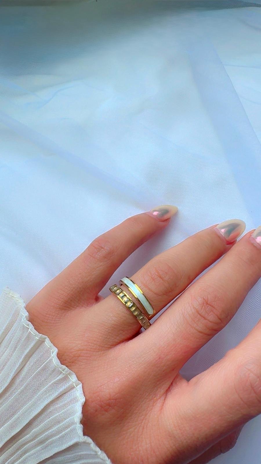 Hand wearing a gold ring with a light blue stone on a white background