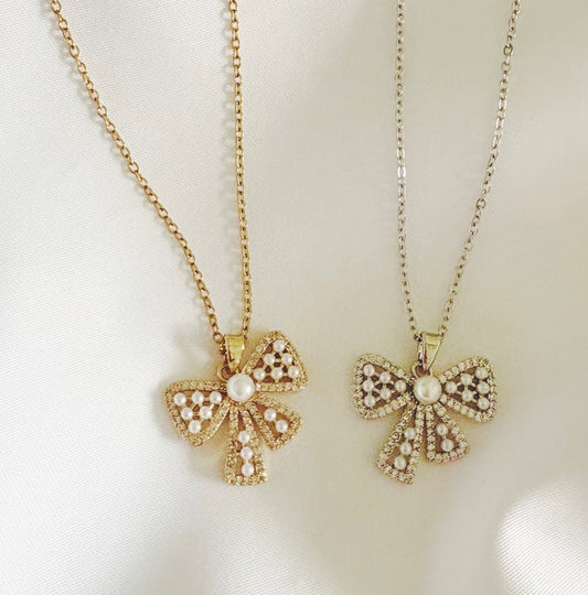 Two gold bow-shaped pendants on chains against a white background