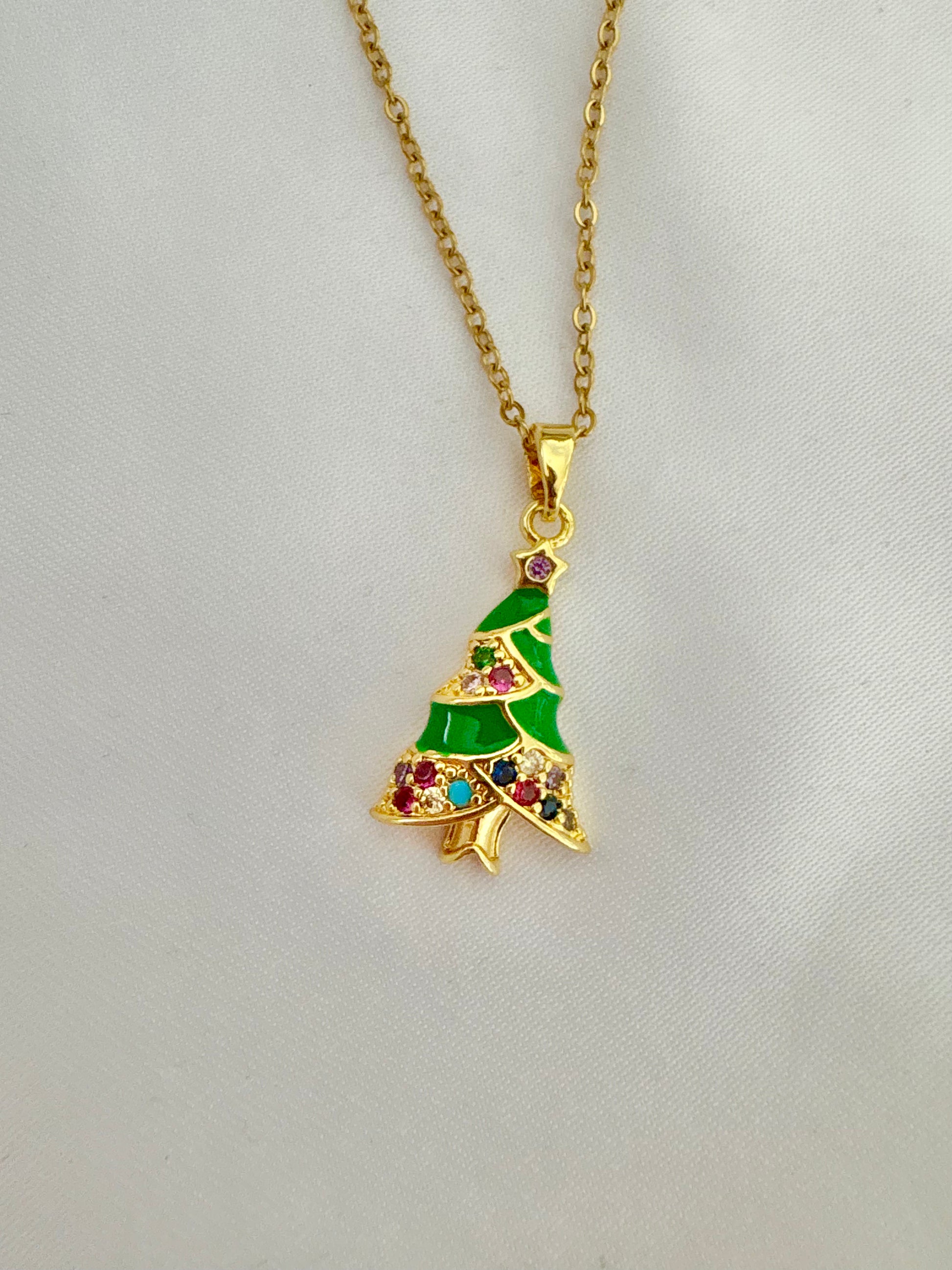 Gold necklace with a green Christmas tree pendant on a light gray background.