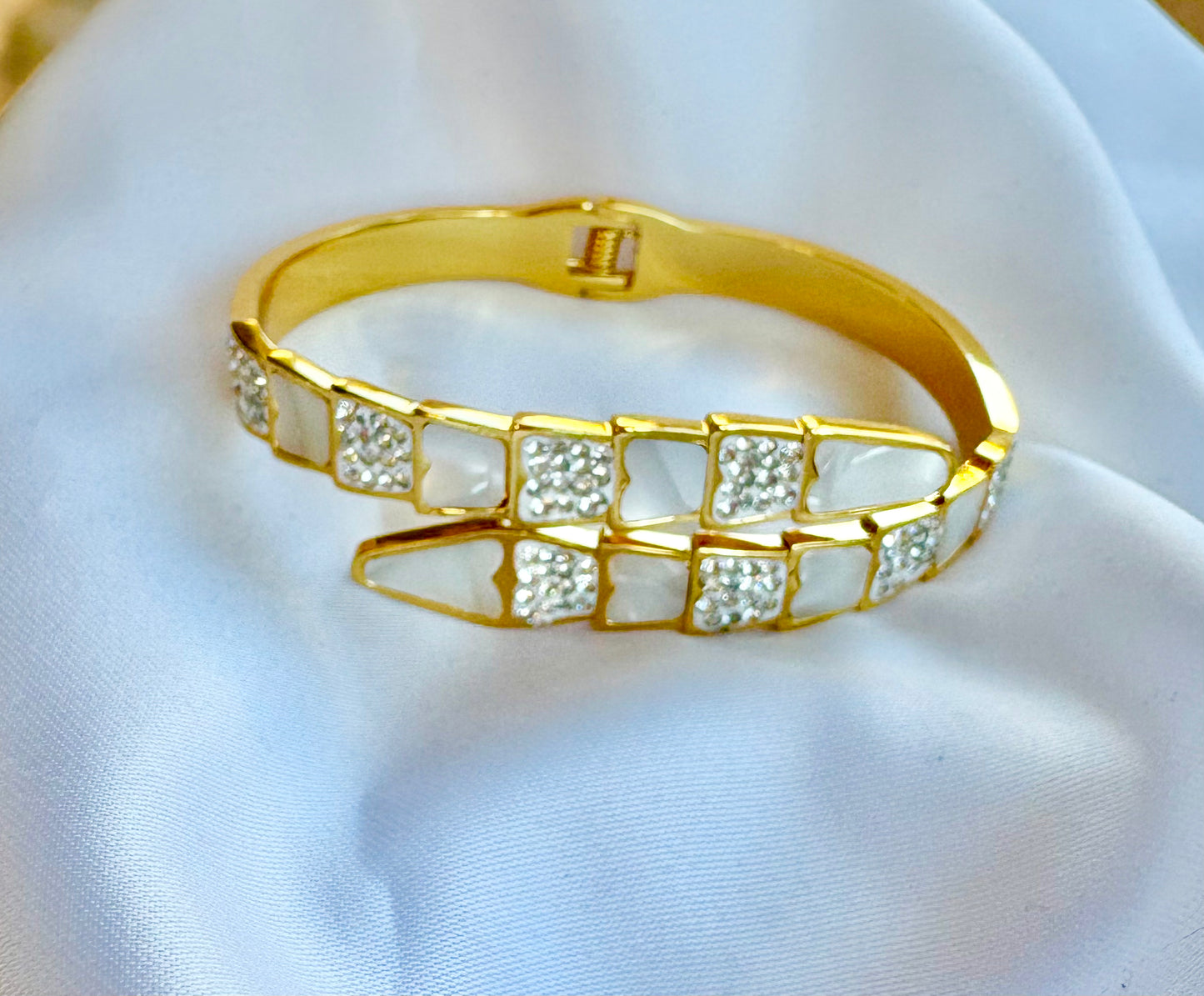 Gold bracelet with embedded stones on a white fabric background