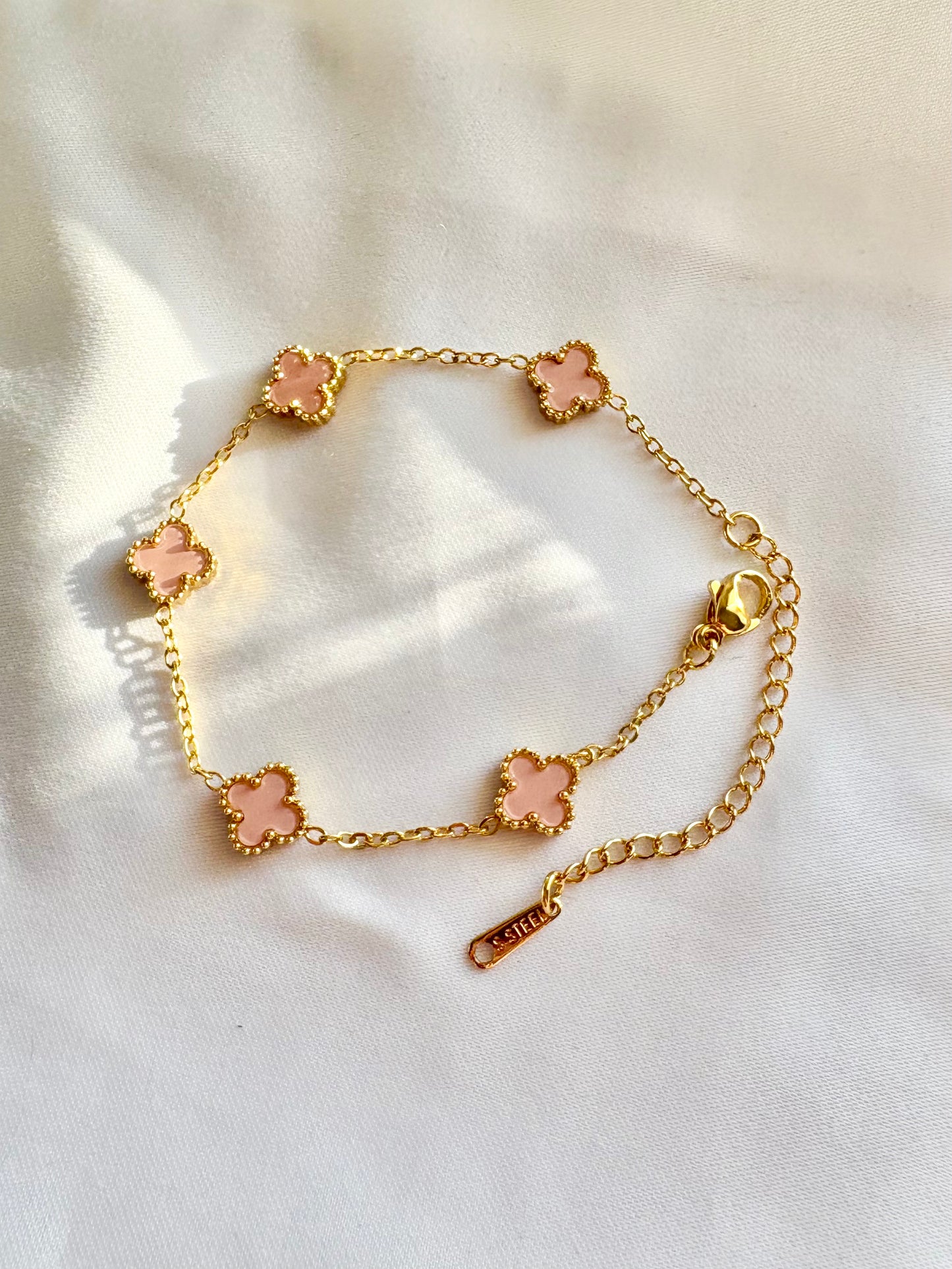 Gold bracelet with pink flower charms on a white fabric background