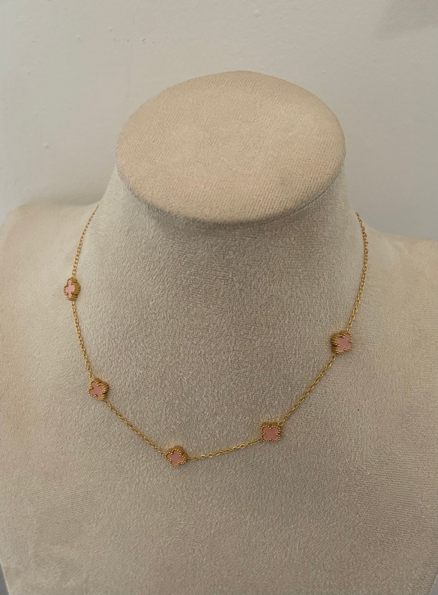 Gold necklace with pink stones on a mannequin bust against a plain background