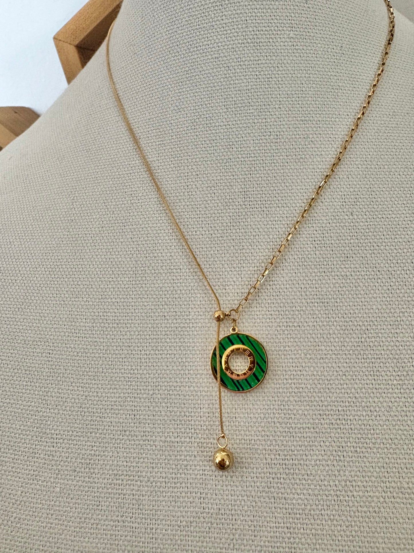 Gold necklace with a green pendant on a mannequin bust.