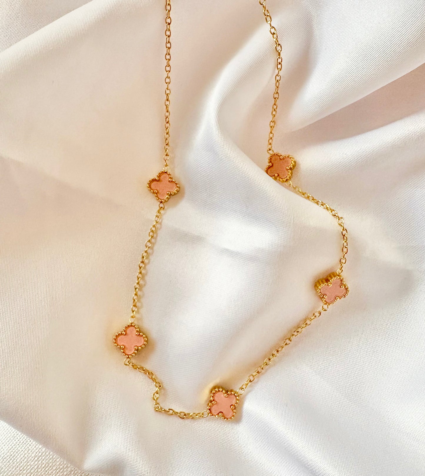 Gold necklace with pink clover-shaped pendants on a white fabric background
