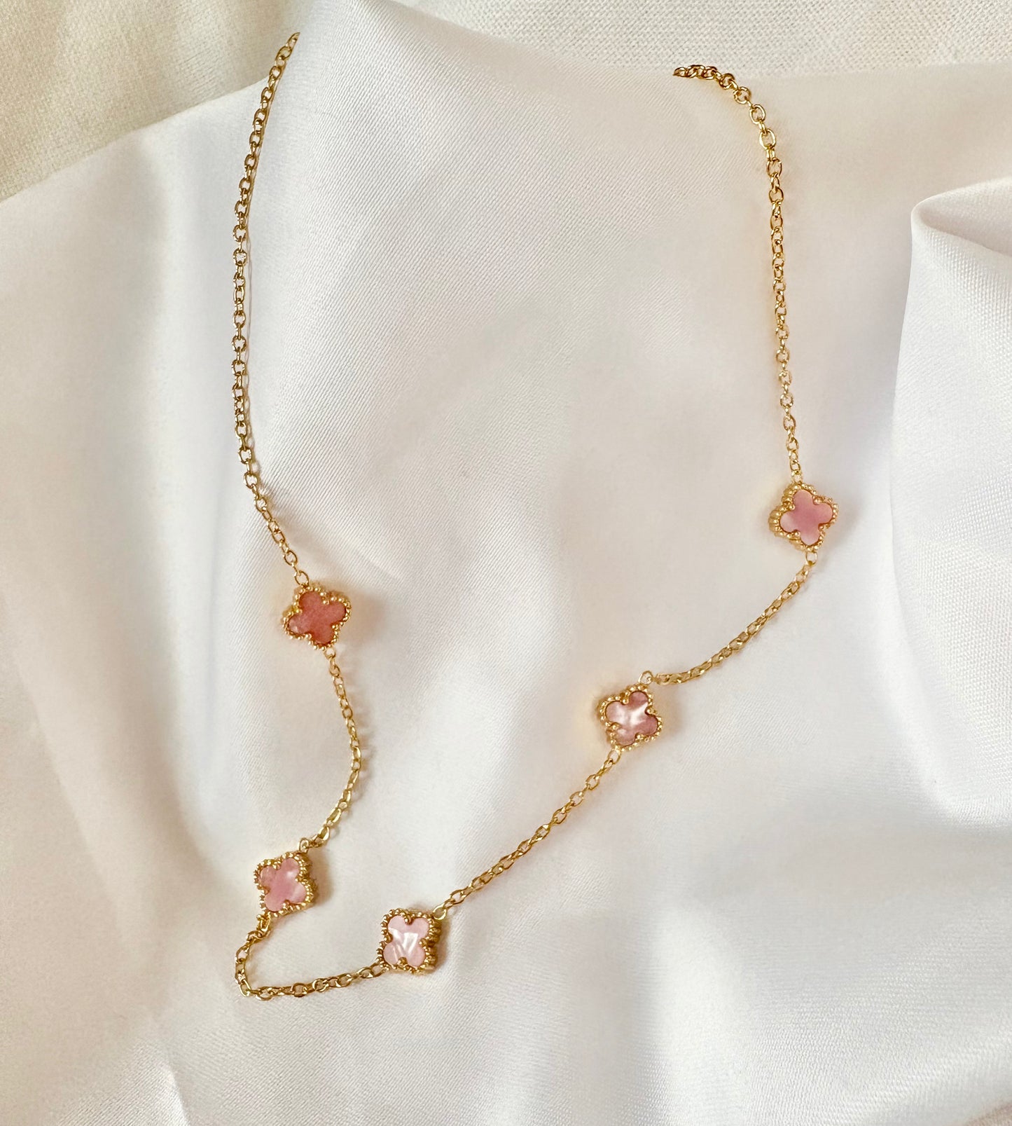 Gold necklace with glossy pink flower pendants on a white fabric background