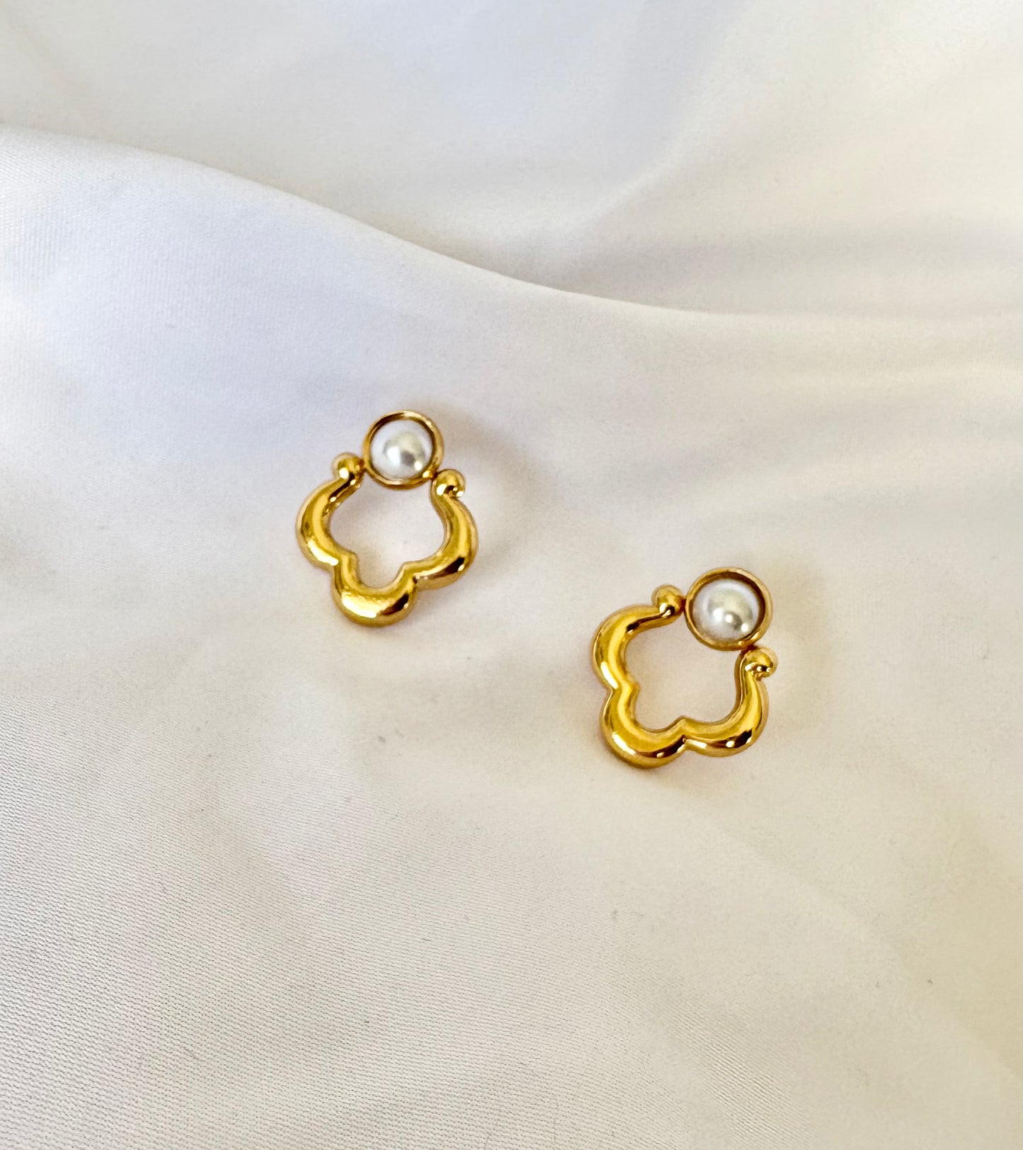 Gold clover pearl earrings displayed on fabric background
