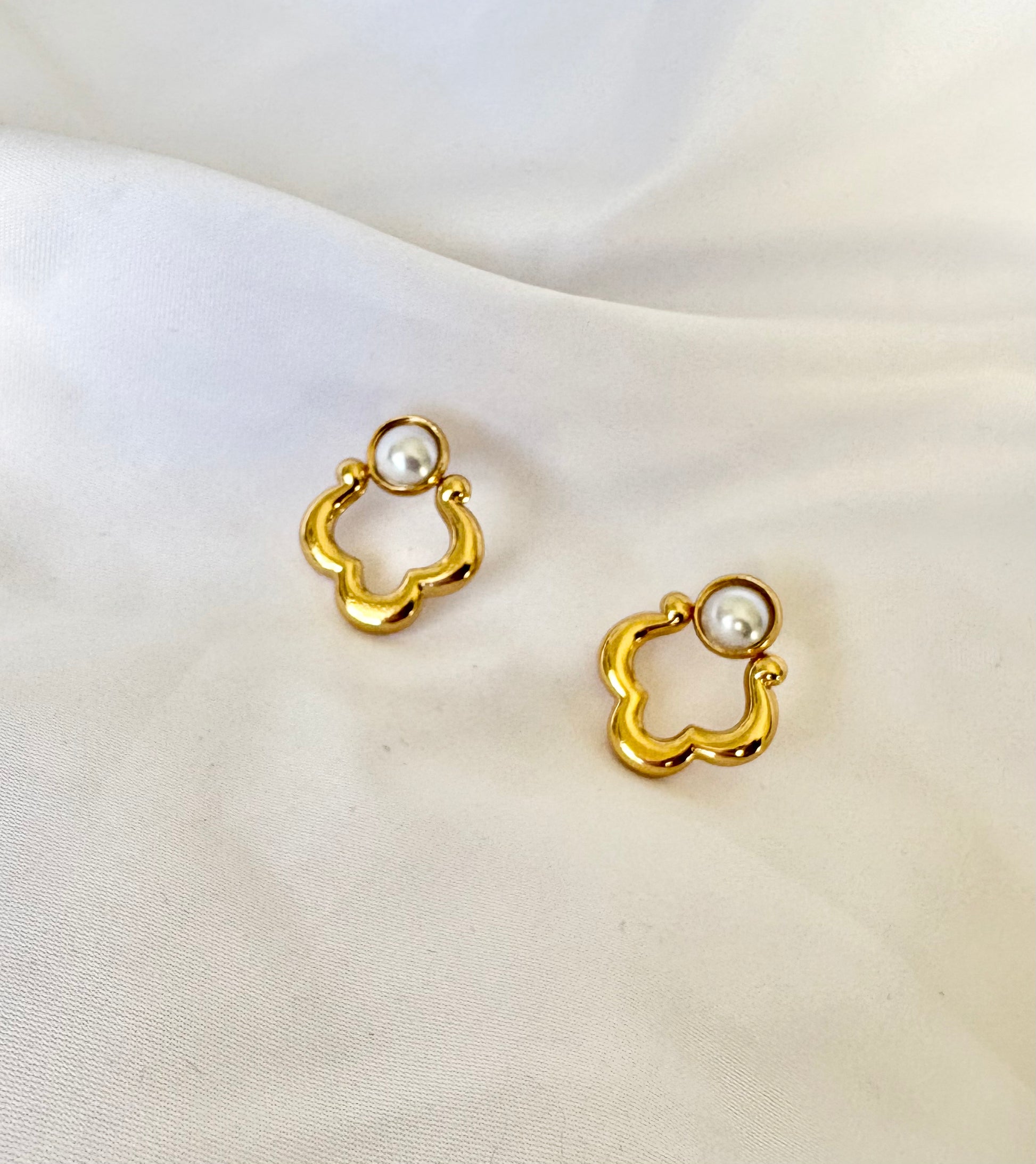 Gold clover pearl earrings displayed on fabric background