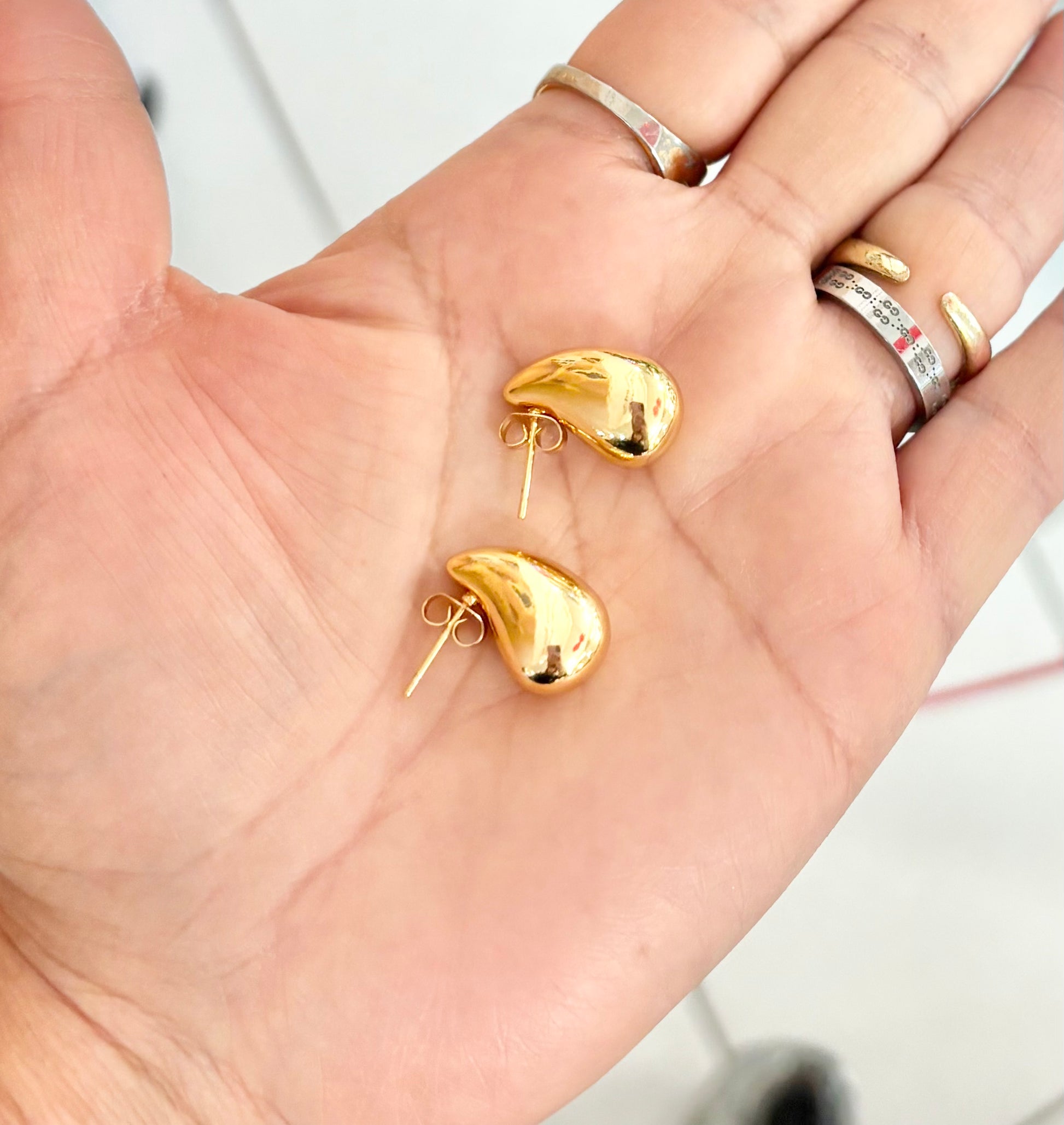 Gold earrings held in a hand with a plain background
