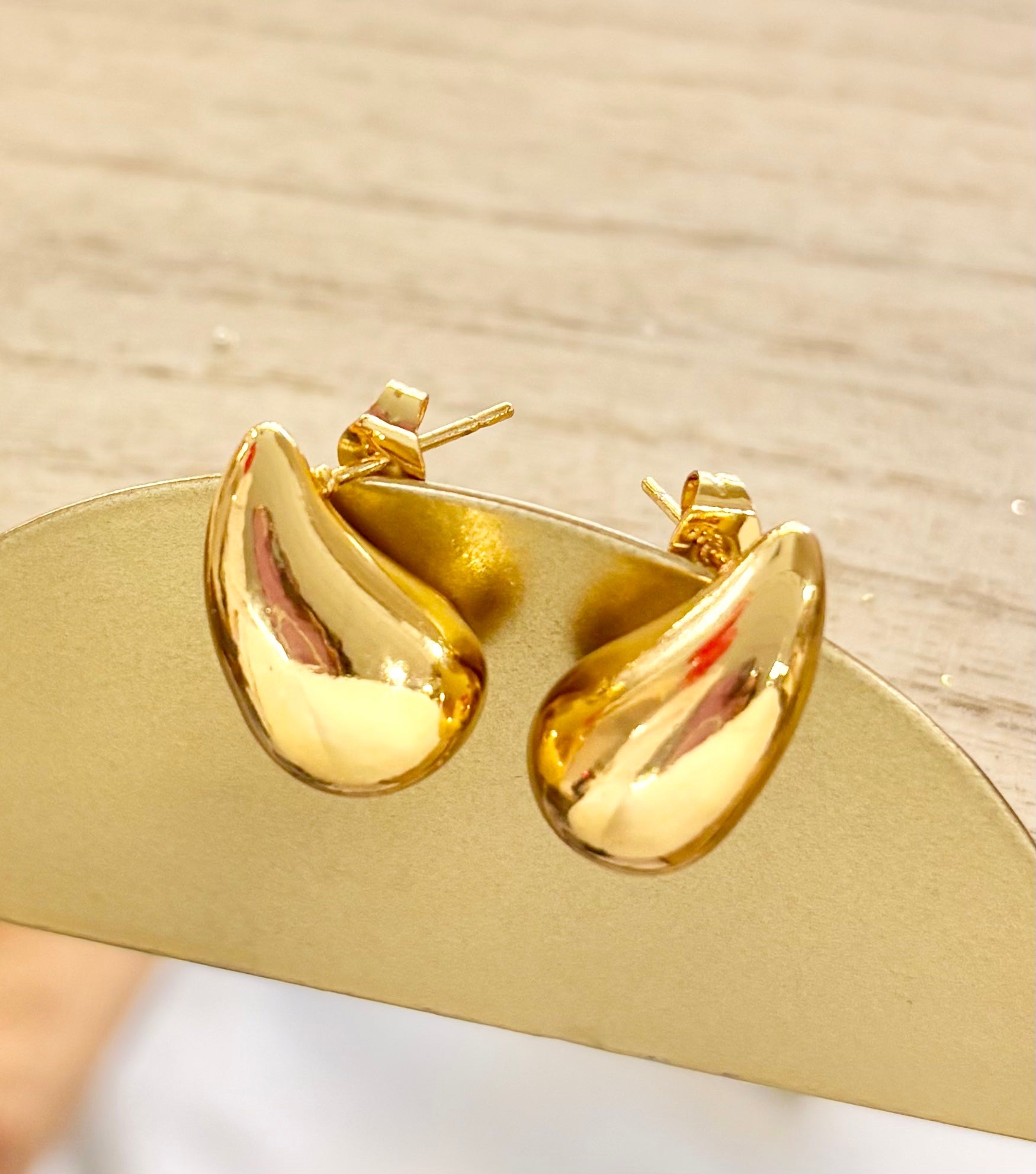 Gold hoop earrings on a gold stand with a neutral background