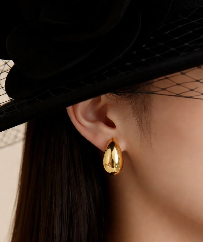 Gold hoop earrings worn by a person with a black hat and veil.