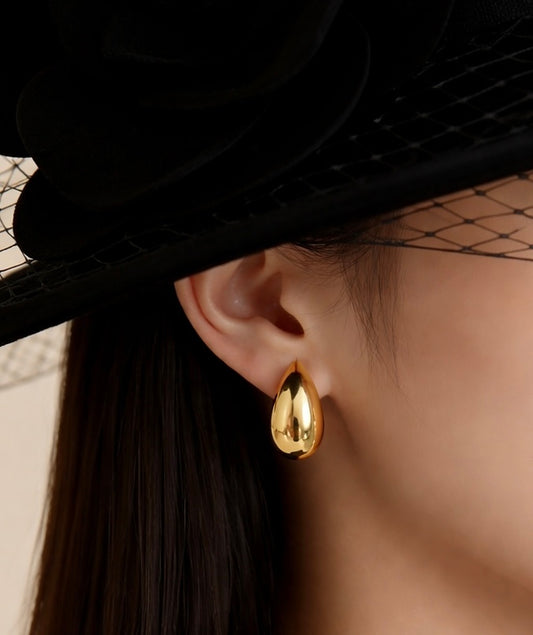 Gold hoop earrings worn by a person with a black hat and veil.