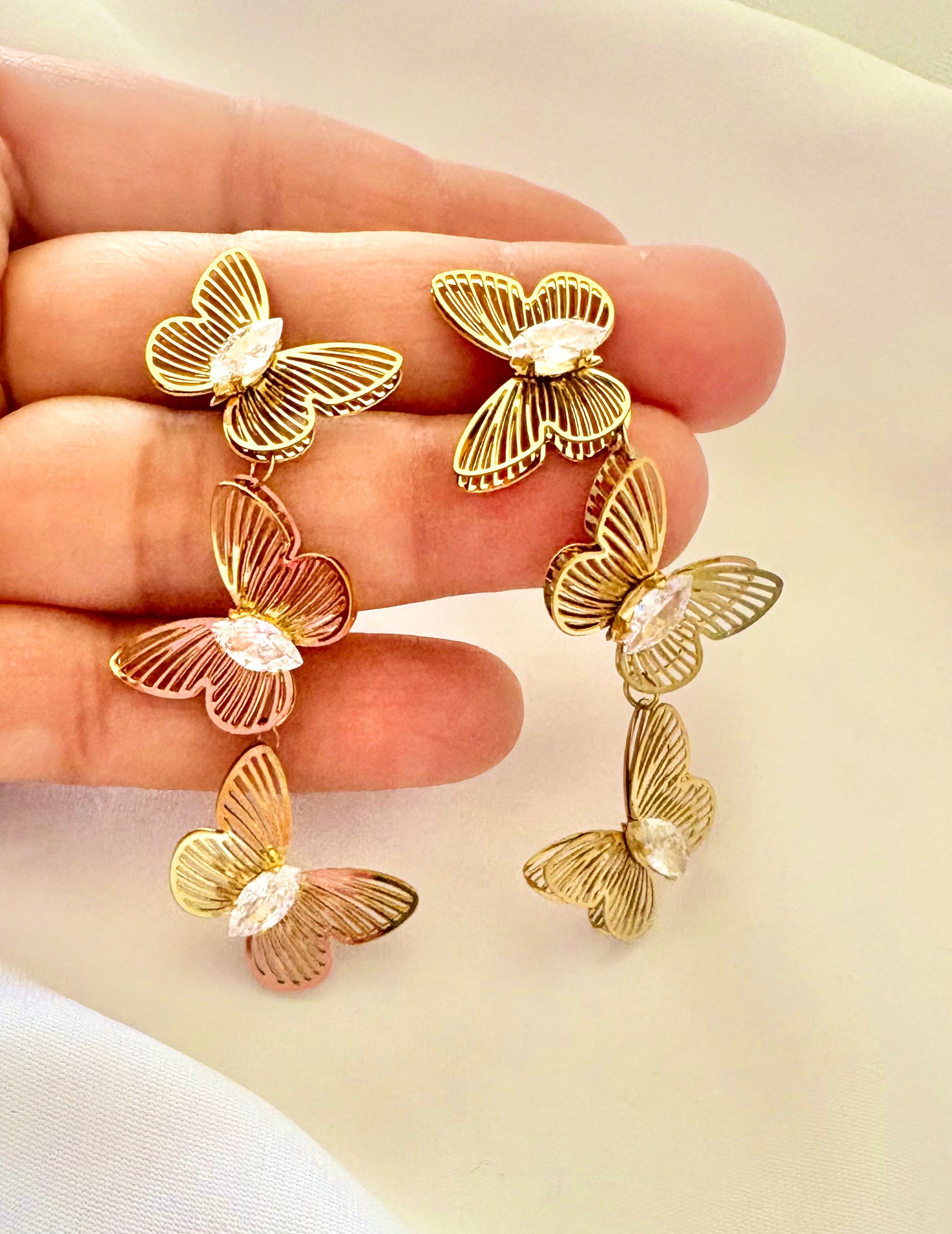 Butterfly-shaped earrings held in a hand against a light background