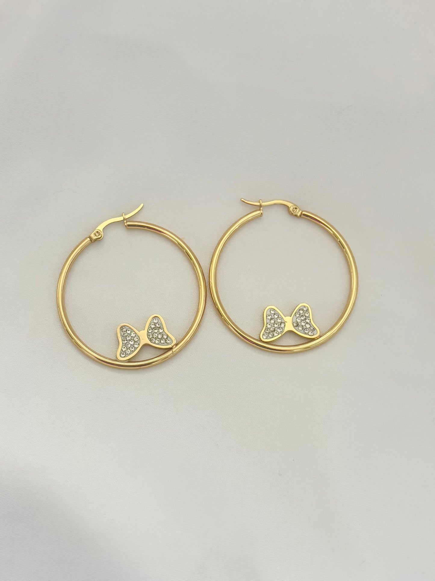Gold hoop earrings with bow designs on a light gray background