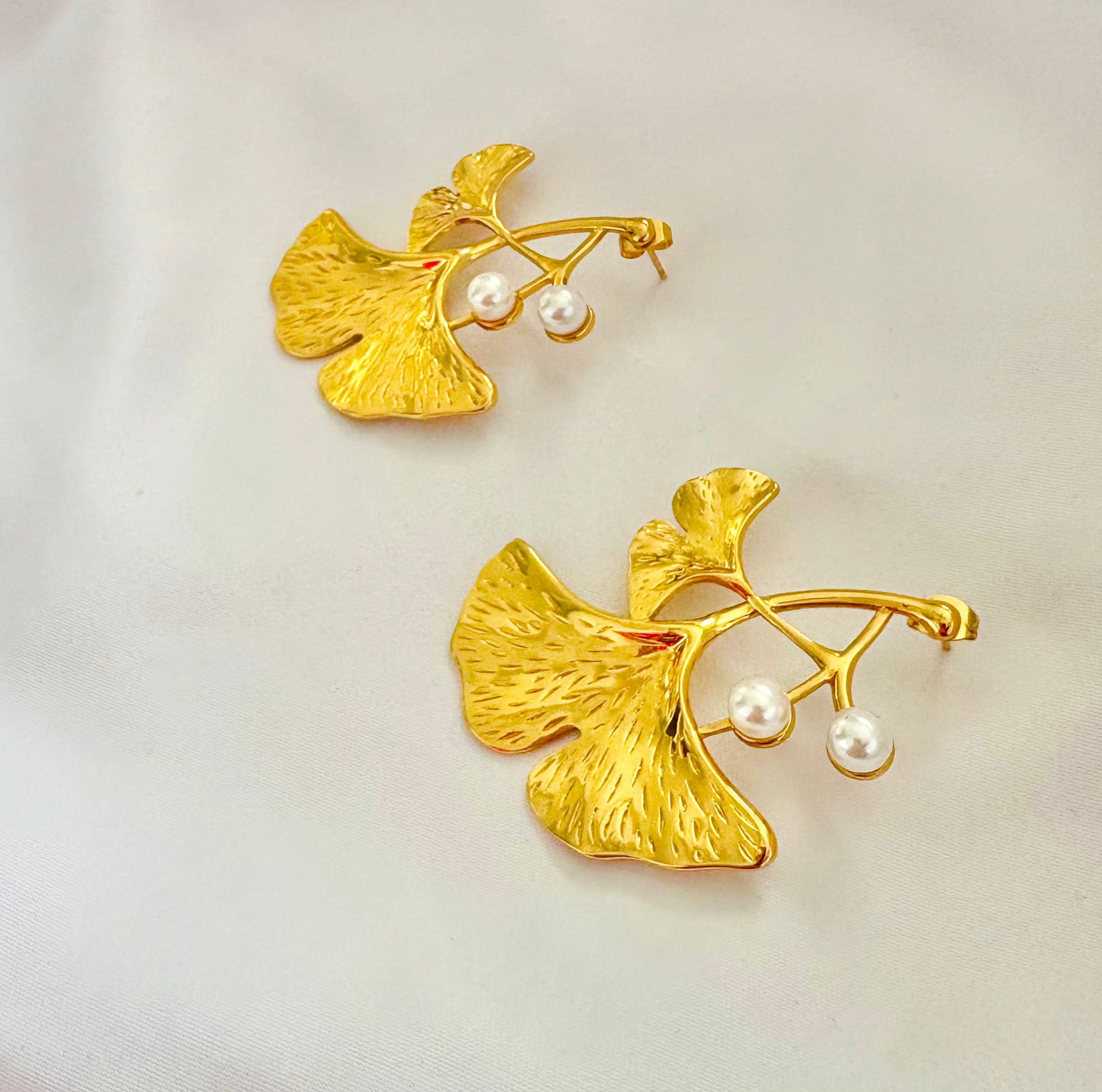 Gold leaf-shaped earrings with pearl-like beads on a light background