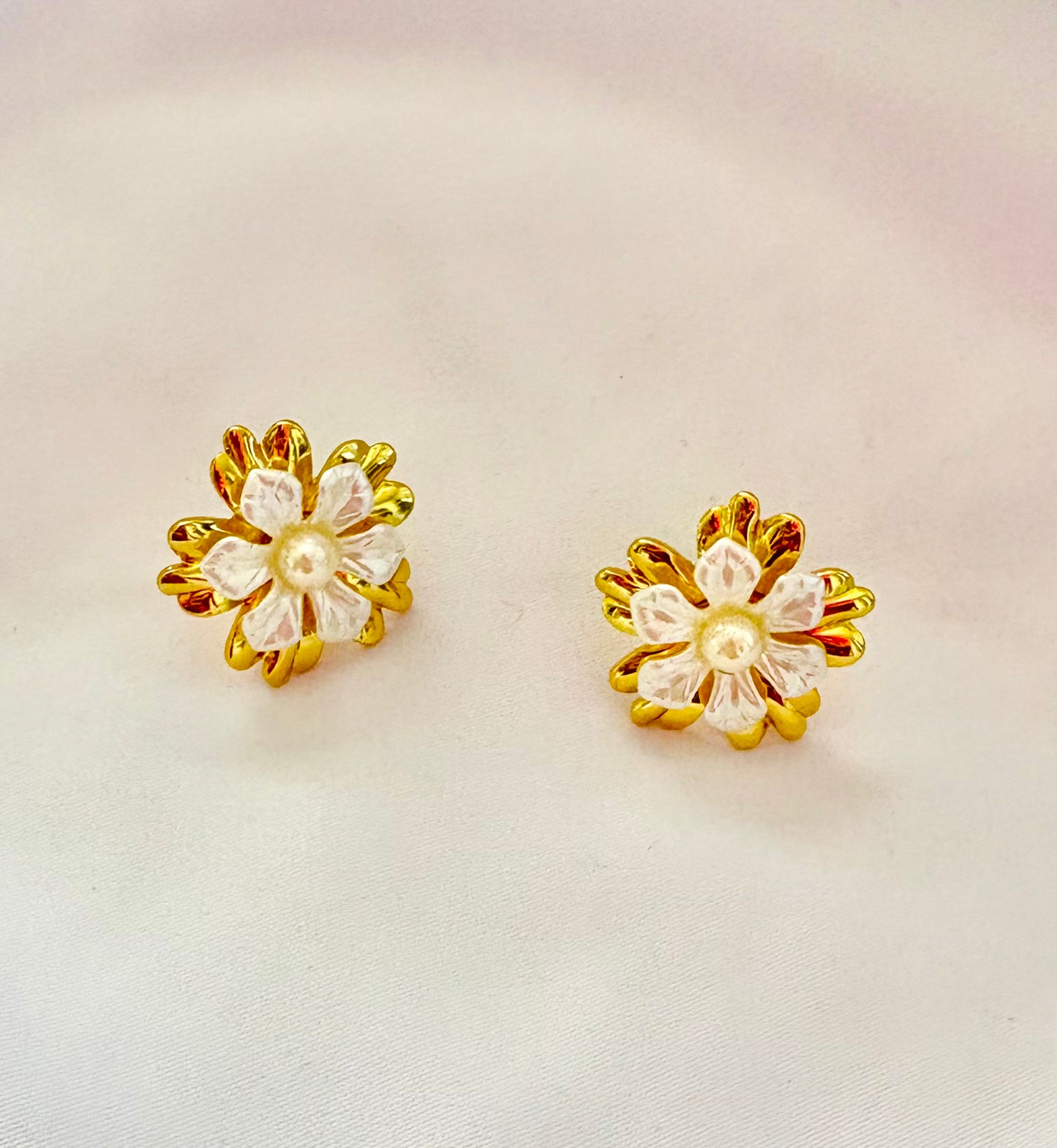 Pair of gold and white flower-shaped earrings on a light background