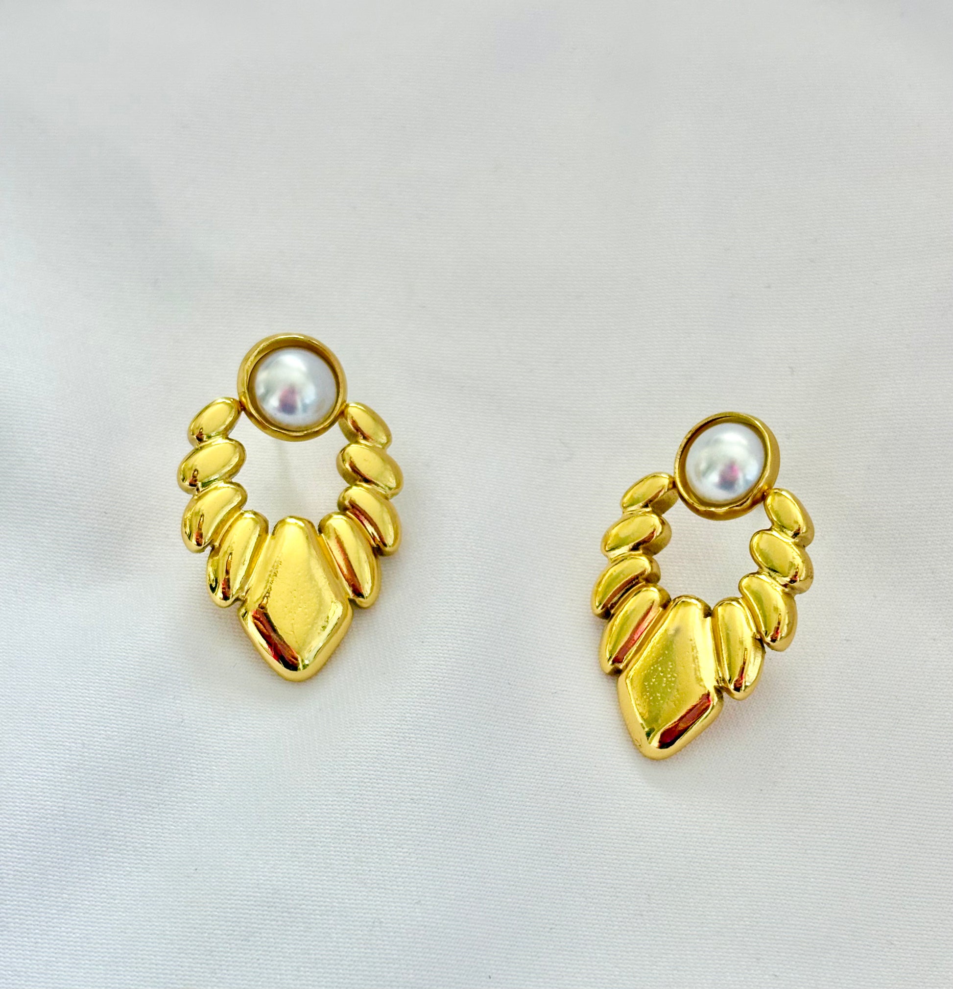 Pair of gold earrings with pearl-like centers on a light gray background