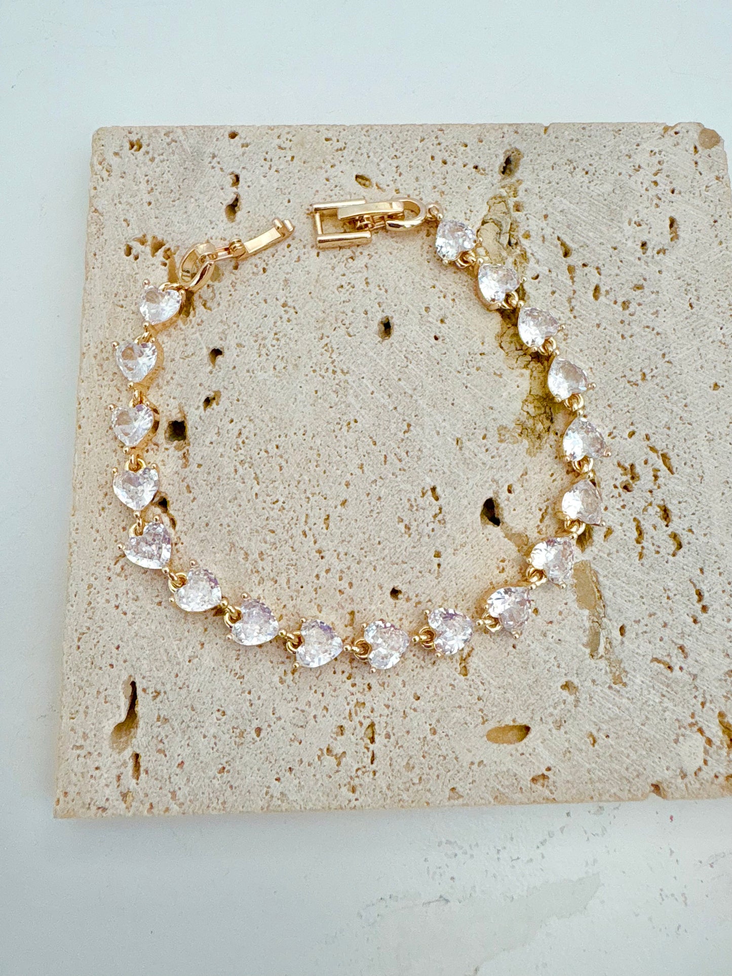 Gold bracelet with clear heart-shaped stones on a textured stone surface