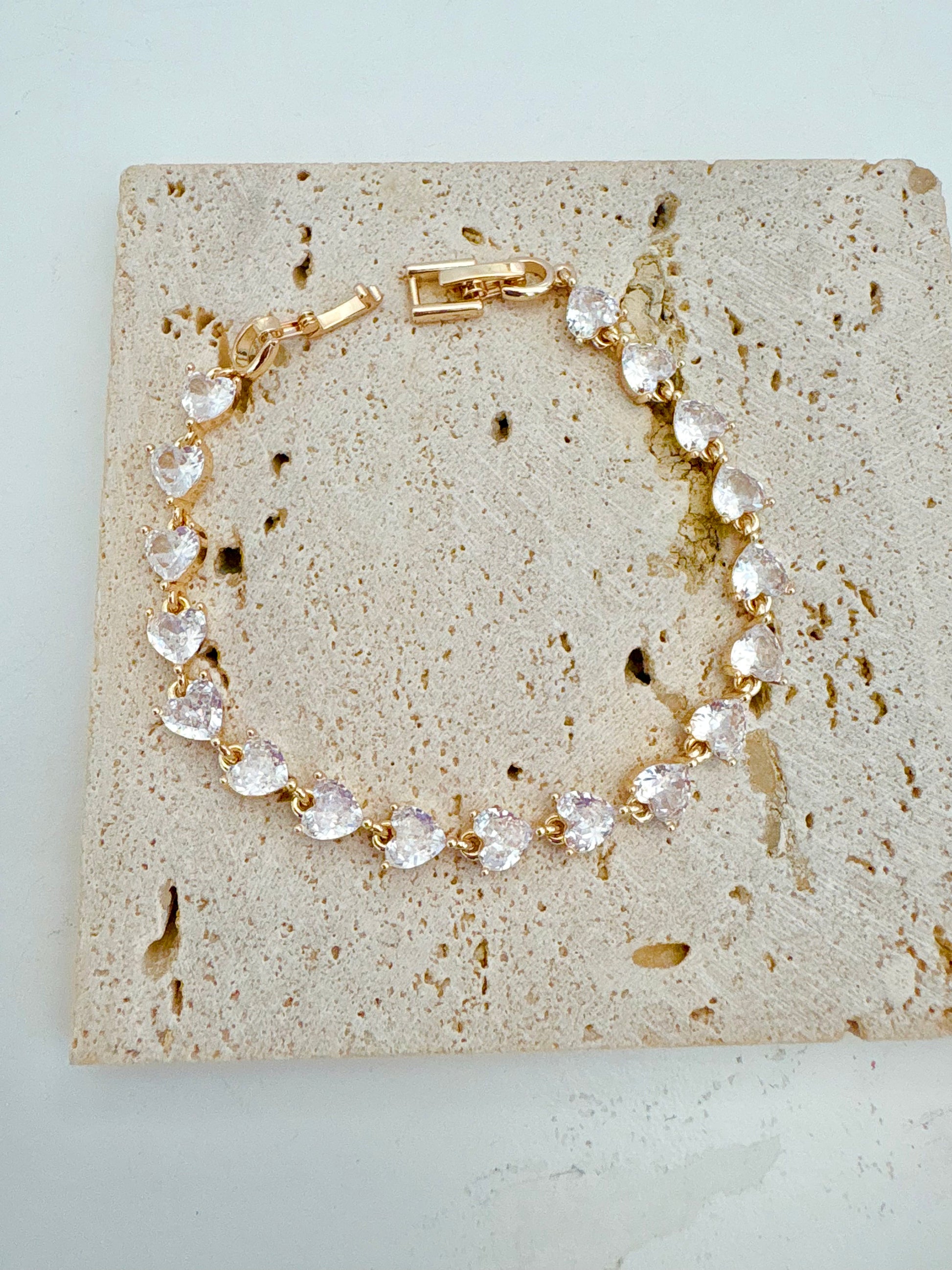 Gold bracelet with clear heart-shaped stones on a textured stone surface