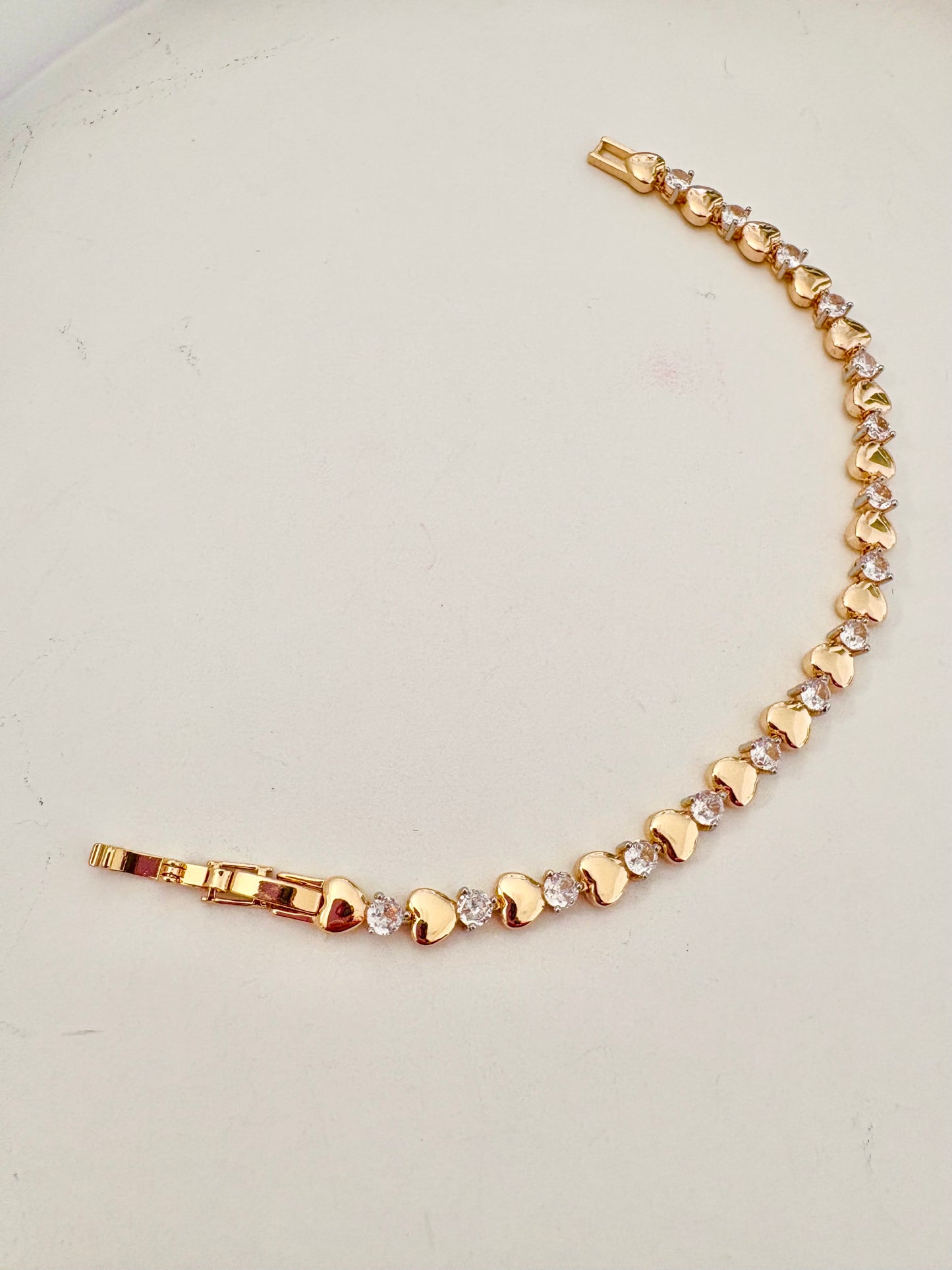 Gold bracelet with heart-shaped links on a light gray background
