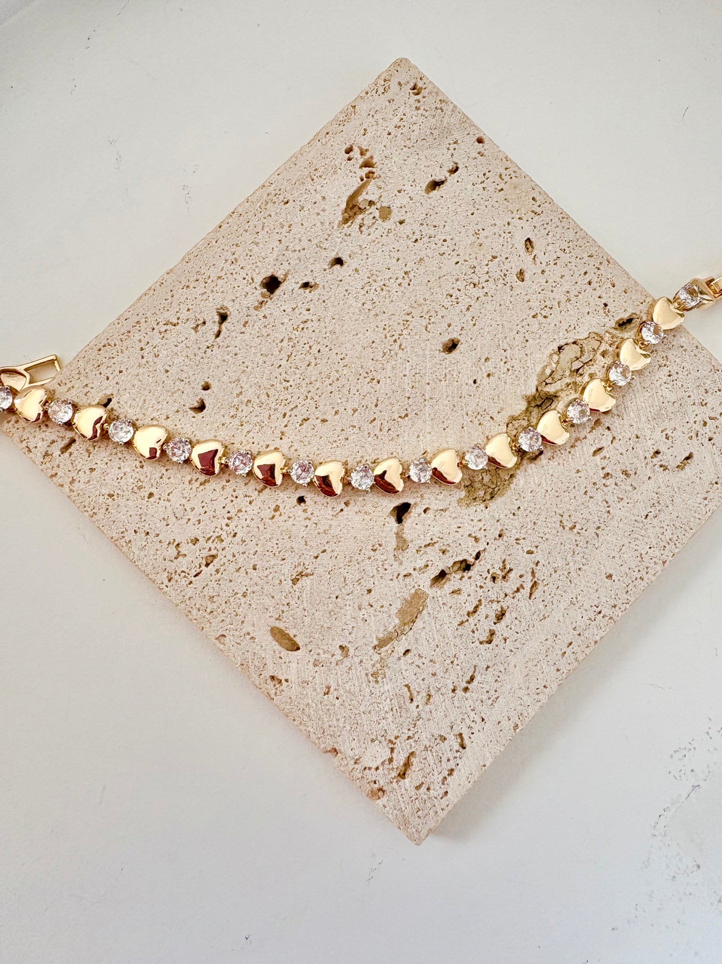 Gold bracelet with heart-shaped beads on a textured beige surface