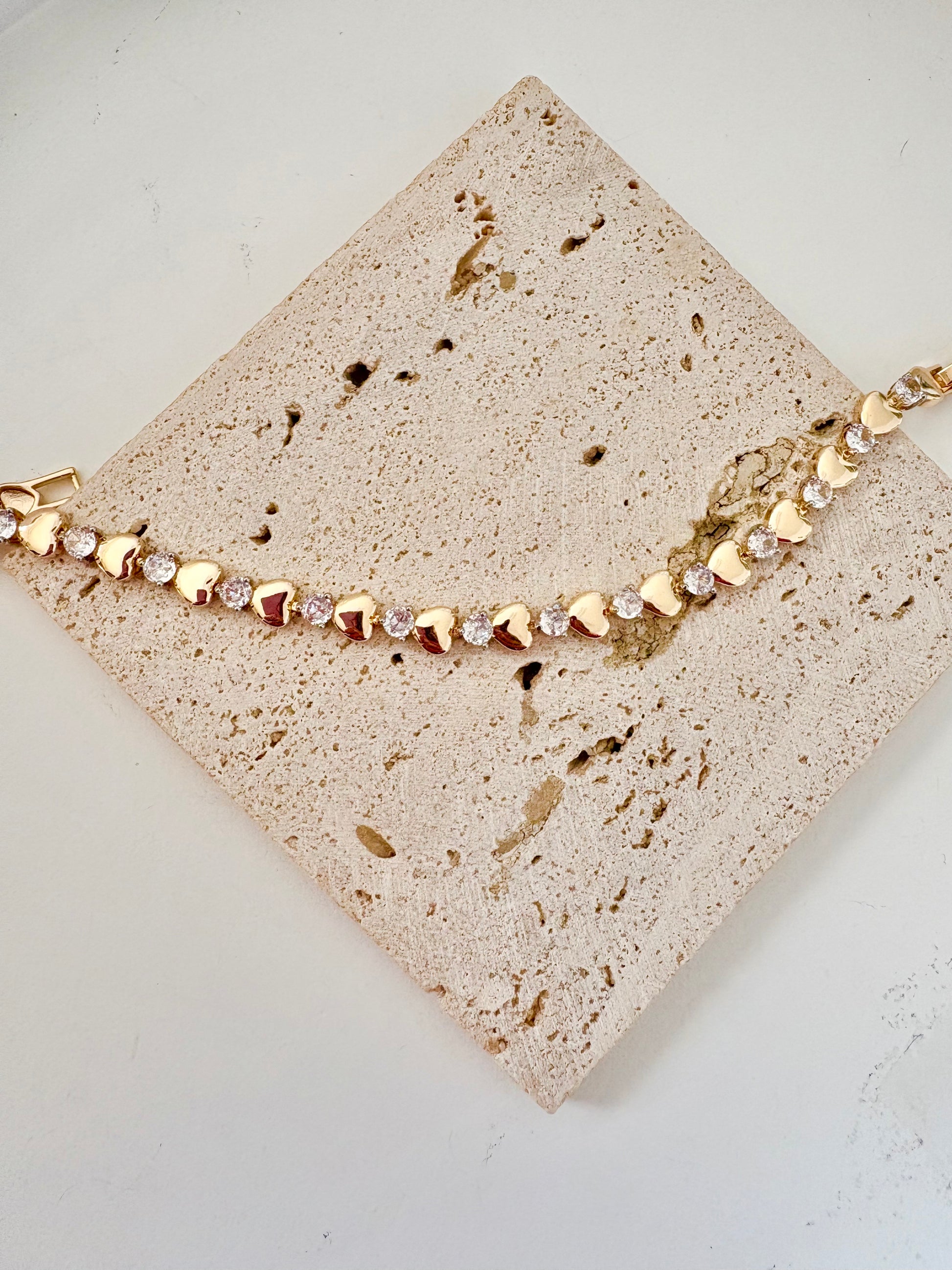 Gold bracelet with heart-shaped beads on a textured beige surface