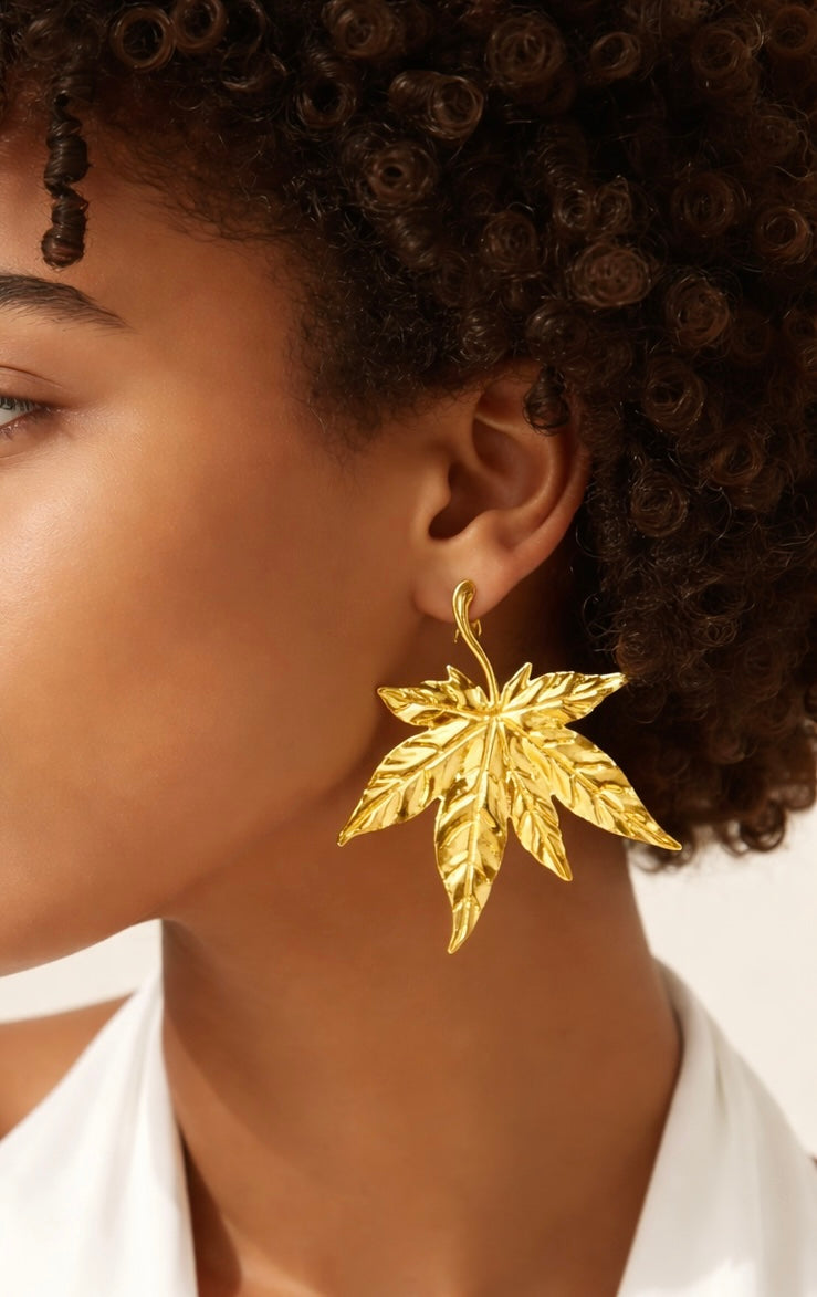 Gold leaf earring worn by a person with white shirt
