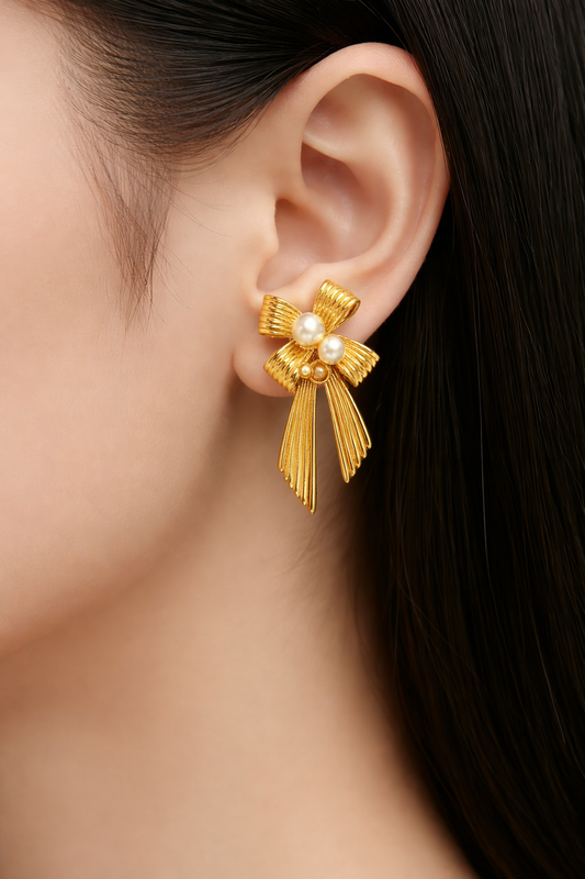 Gold bow-shaped earring with pearls worn by a person