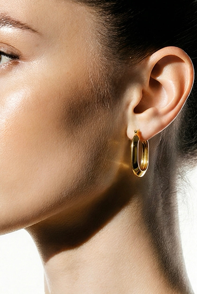 Close-up of a person wearing a gold hoop earring on a neutral background