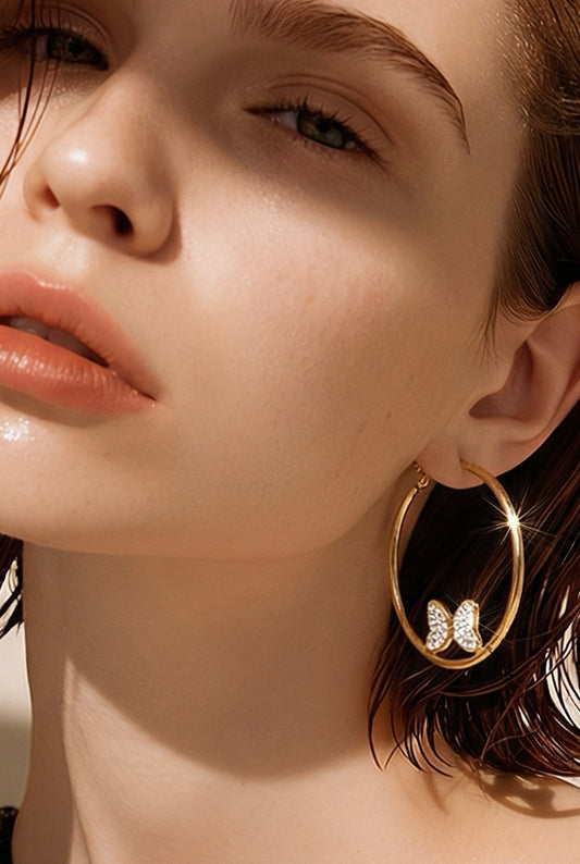 Close-up of a person wearing gold hoop earrings with butterfly charms.